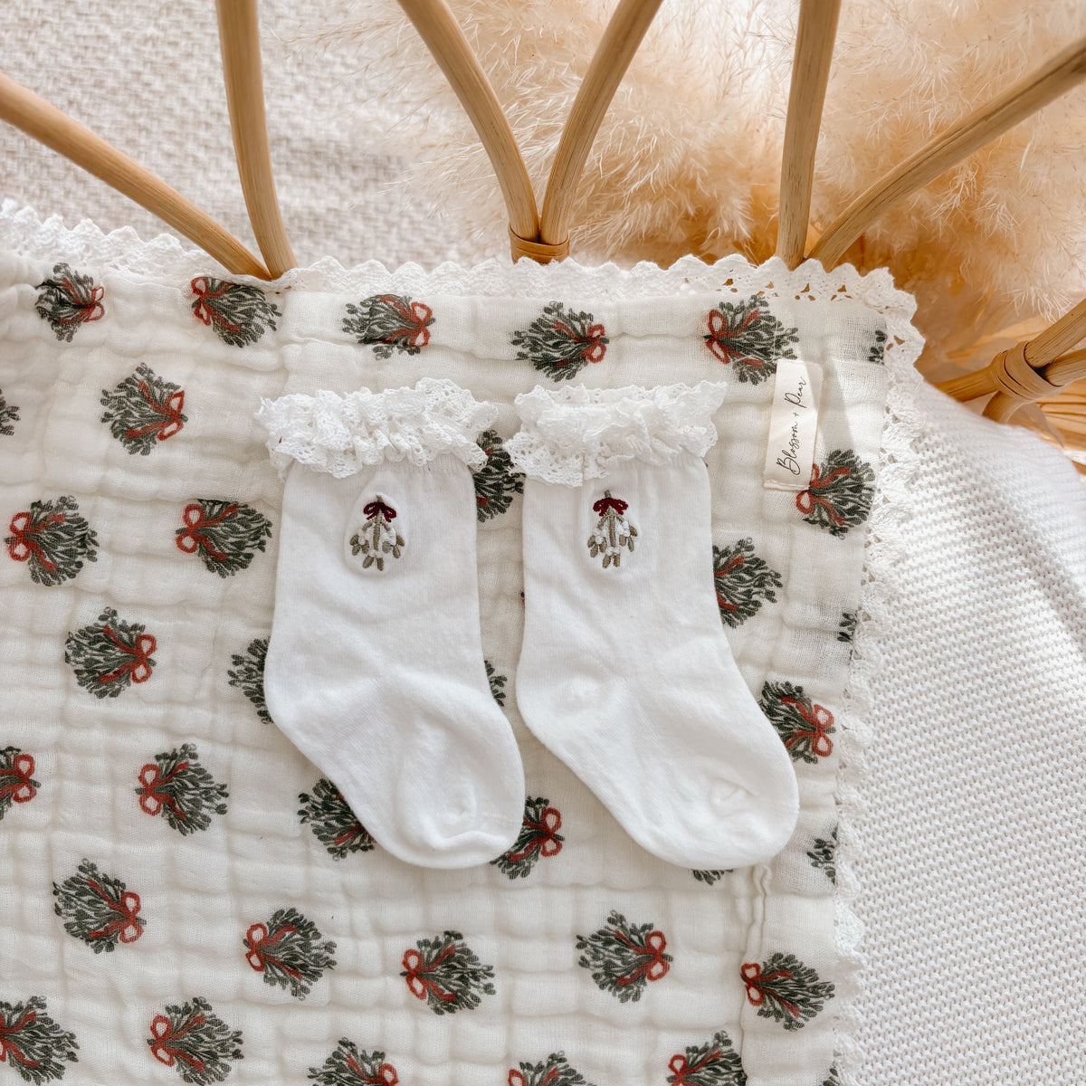 Pair of white baby socks with lace trim, embroidered with mistletoe and a red bow
