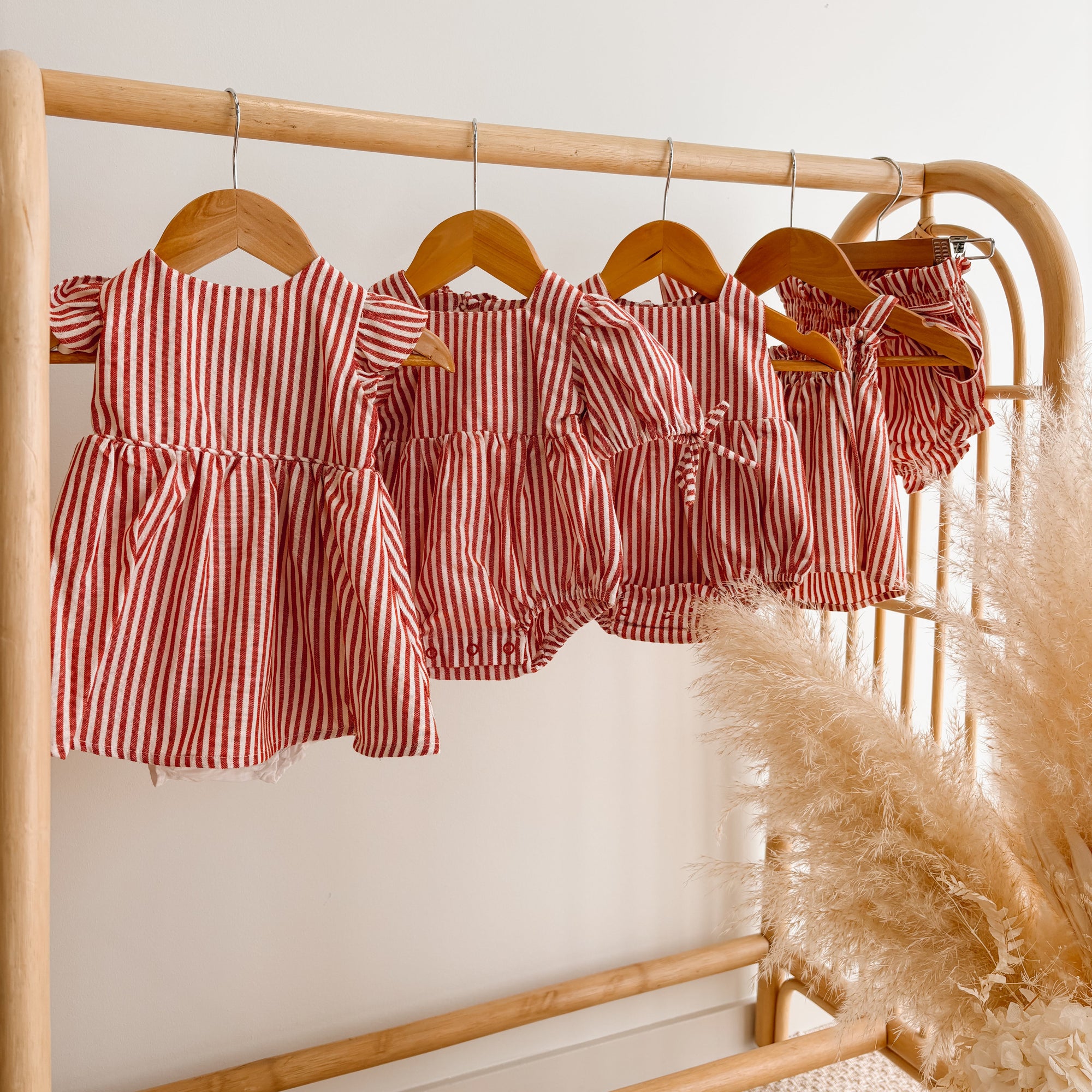 Red stripe Christmas dress, romper and bloomer sets hanging together on a rattan rail