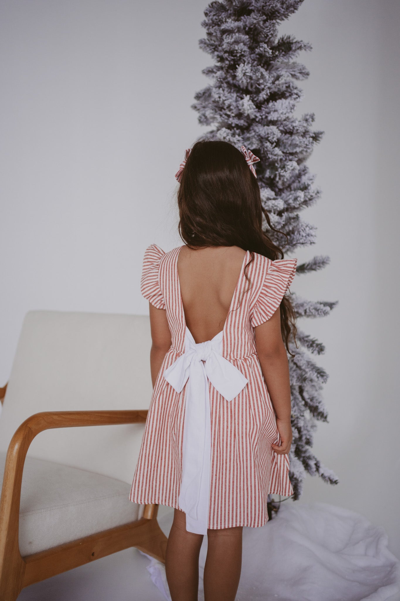 Back view of a girl in a red stripe Christmas dress with a large white bow tie and flutter sleeves