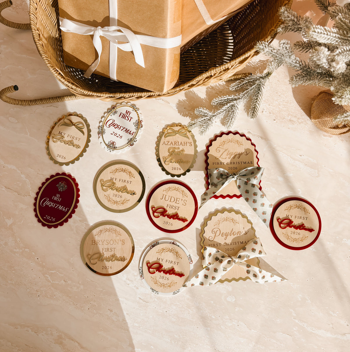 A styled flat-lay of Christmas gift tags and wrapped presents on a beige fabric surface. Several round and oval gift tags with red, gold, and cream holiday designs are scattered in front of a woven basket holding two brown kraft-paper wrapped boxes tied with white ribbons.