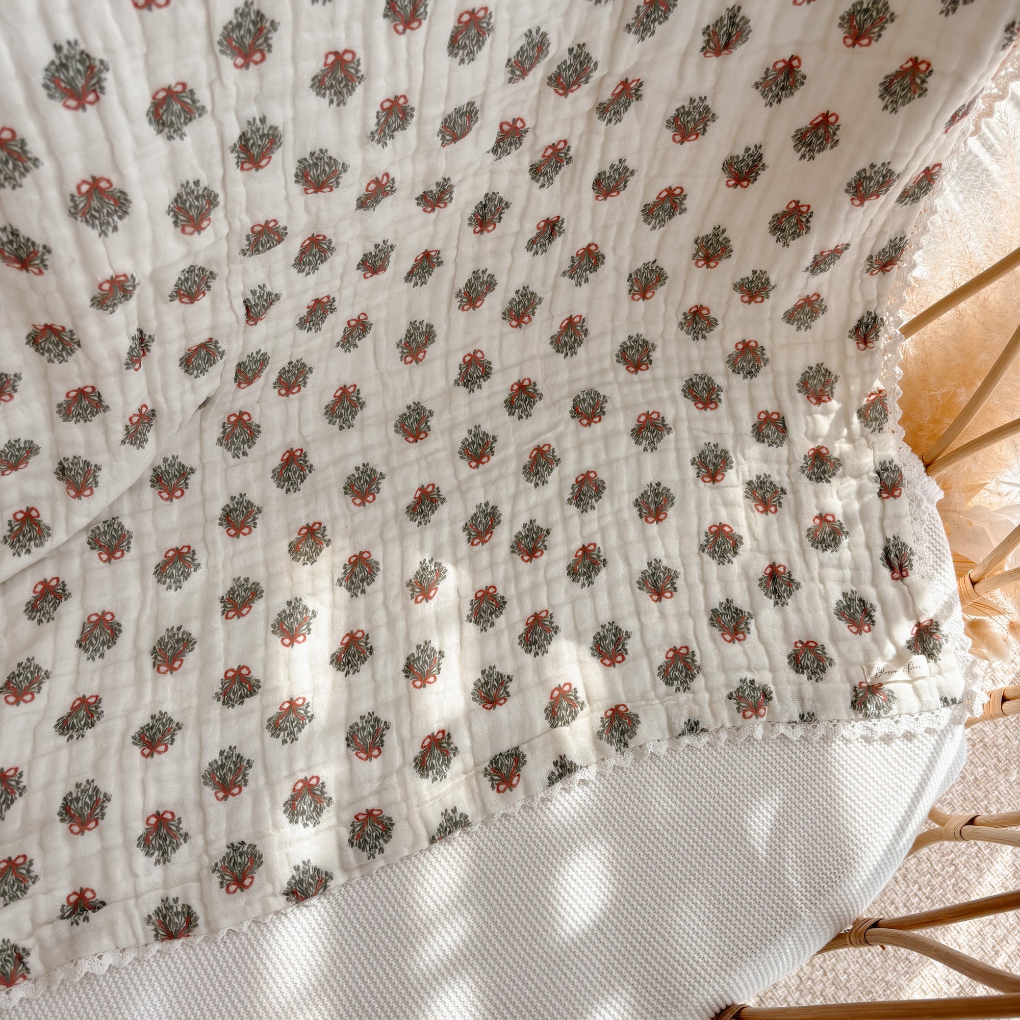 Wreath print muslin baby blanket with scalloped trim draped over a rattan bassinet