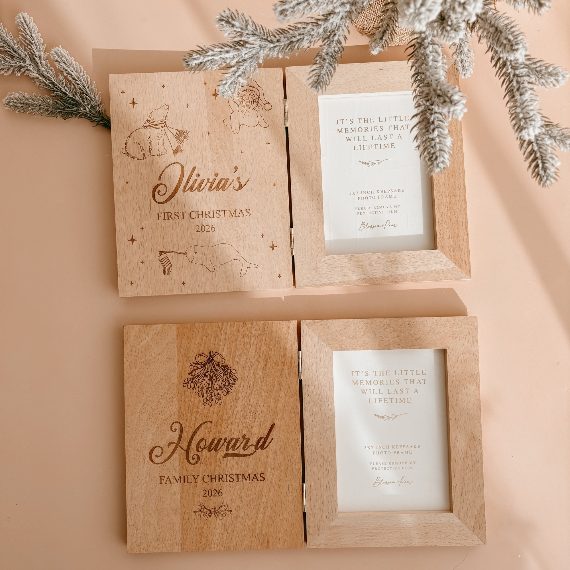 Two personalised wooden keepsake photo frames laid flat, engraved 'Olivia's First Christmas 2026' with polar bear, santa and seal, and 'Howard Family Christmas 2026' with mistletoe, styled with frosted pine