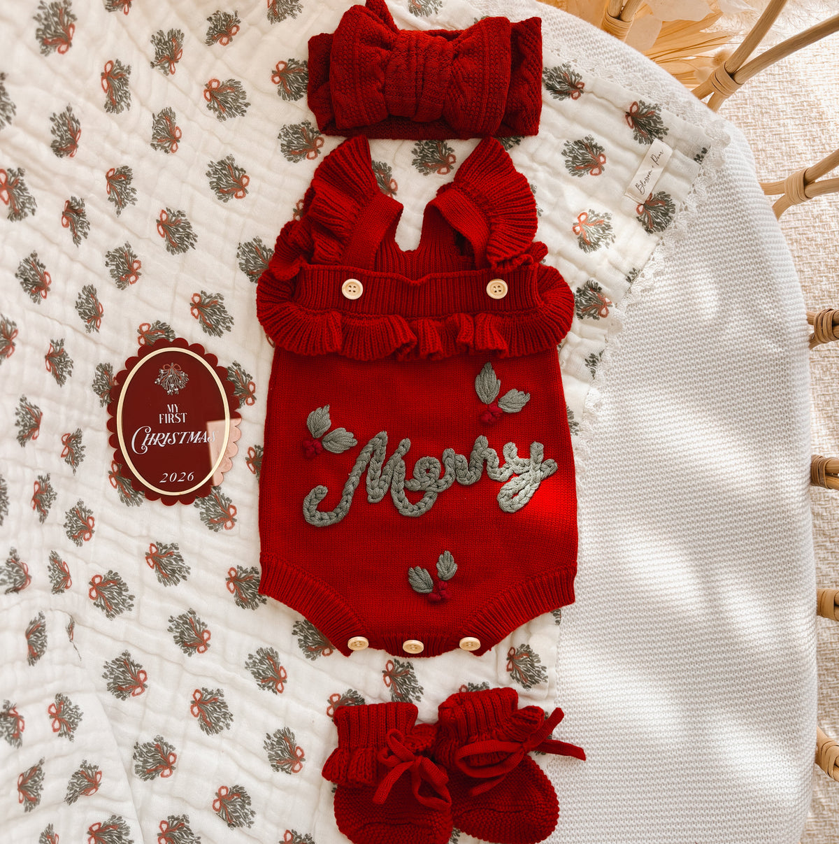 Red Merry knit romper with ruffle trim, styled with a matching red knot headband, red booties and a My First Christmas 2026 keepsake disc