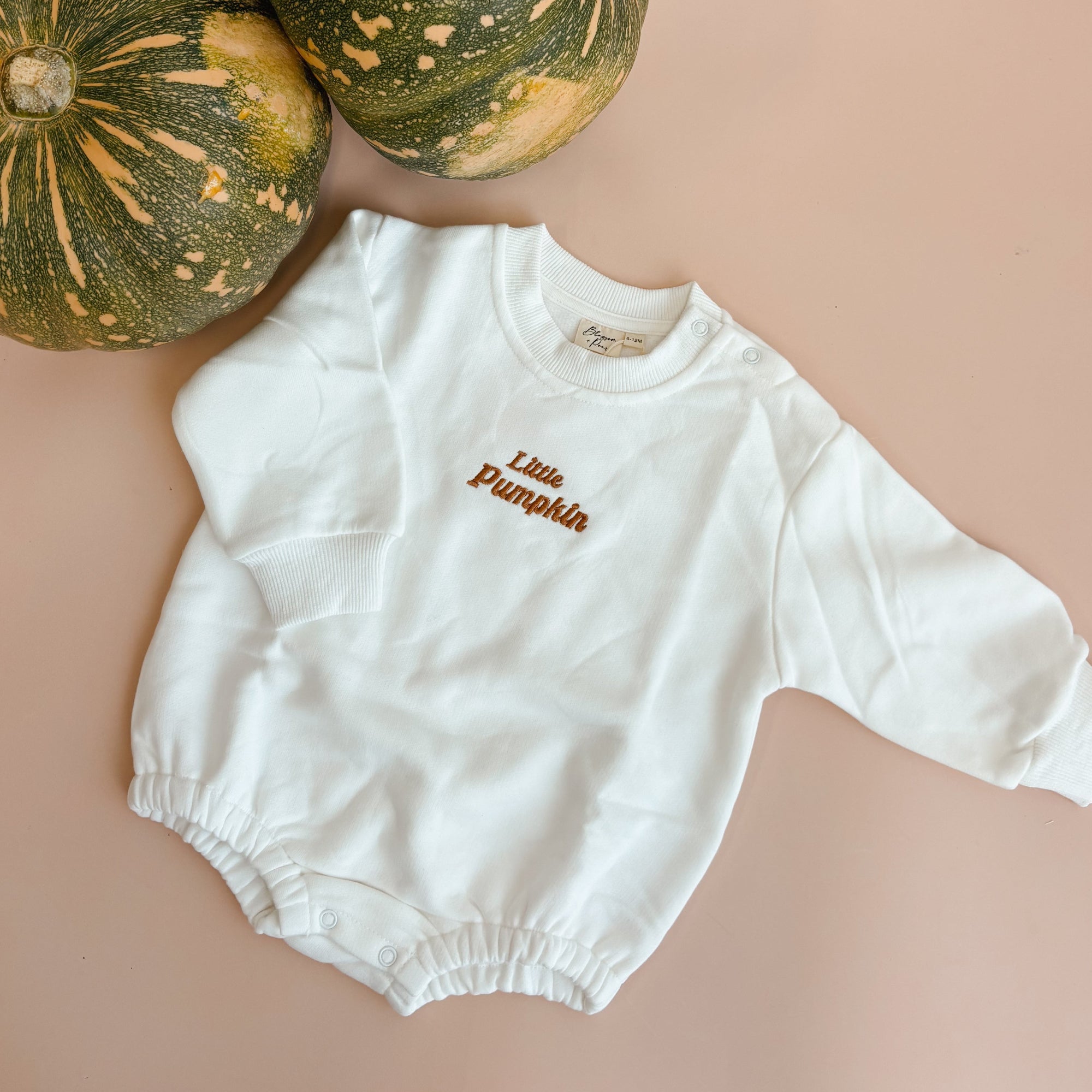 White baby bubble romper embroidered Little Pumpkin in rust thread, styled beside two green pumpkins