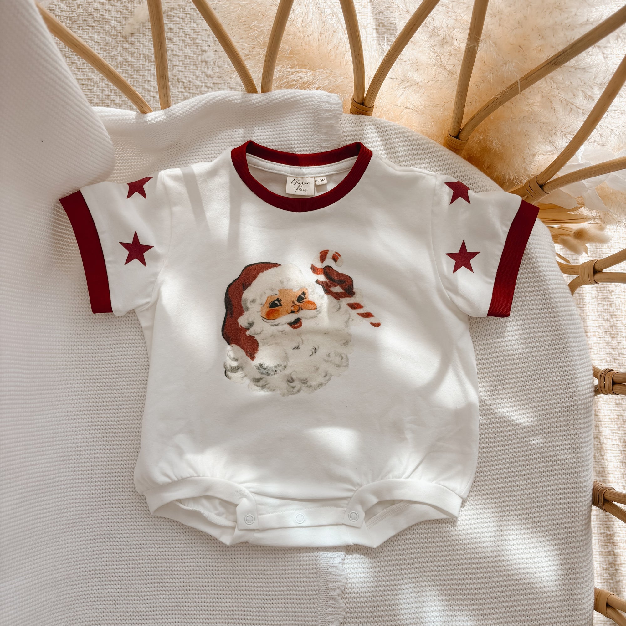 Cream baby romper with a vintage Santa print, red ringer trim and star sleeve detail