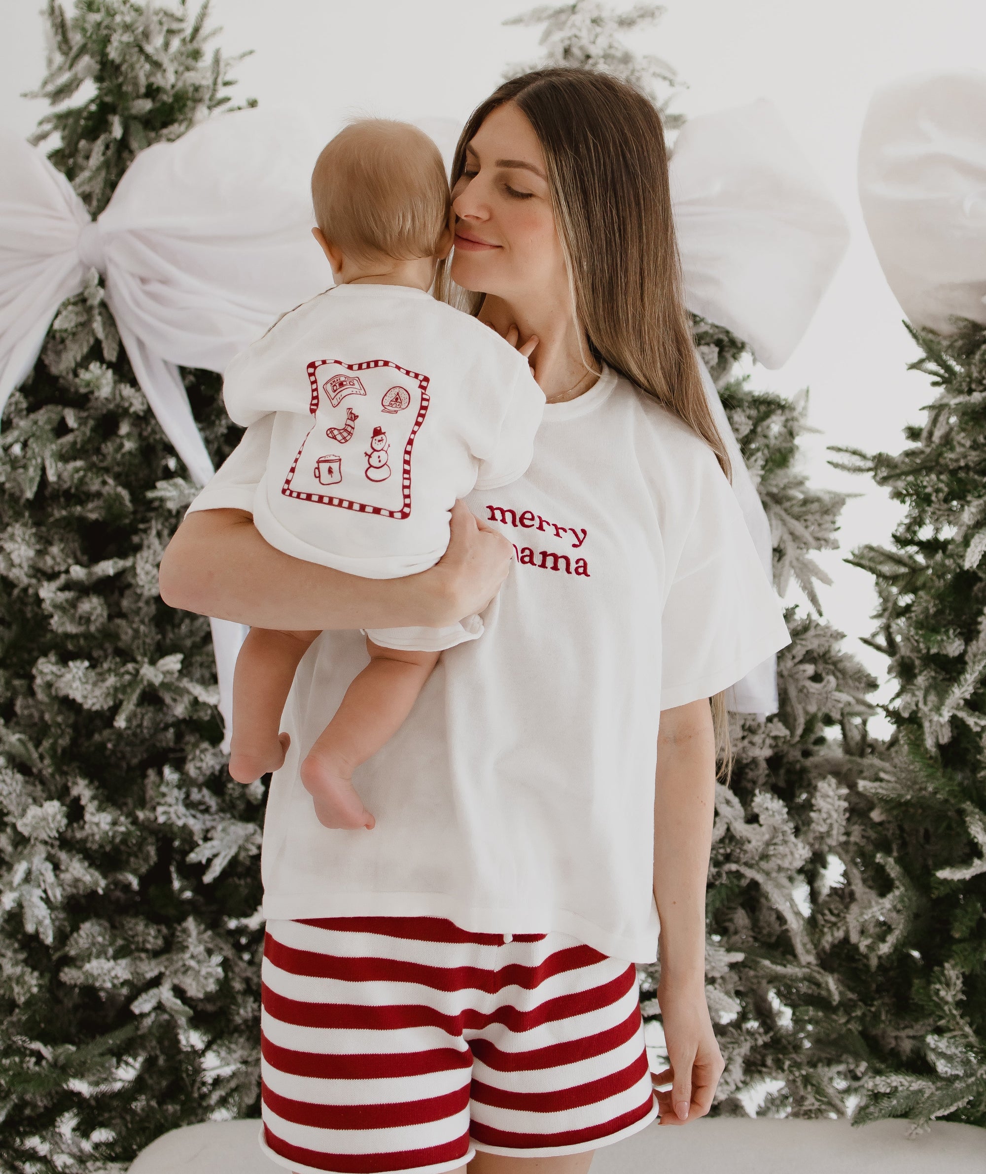 Mum in a merry mama tee holding a baby in a matching Christmas doodle print tee by flocked trees