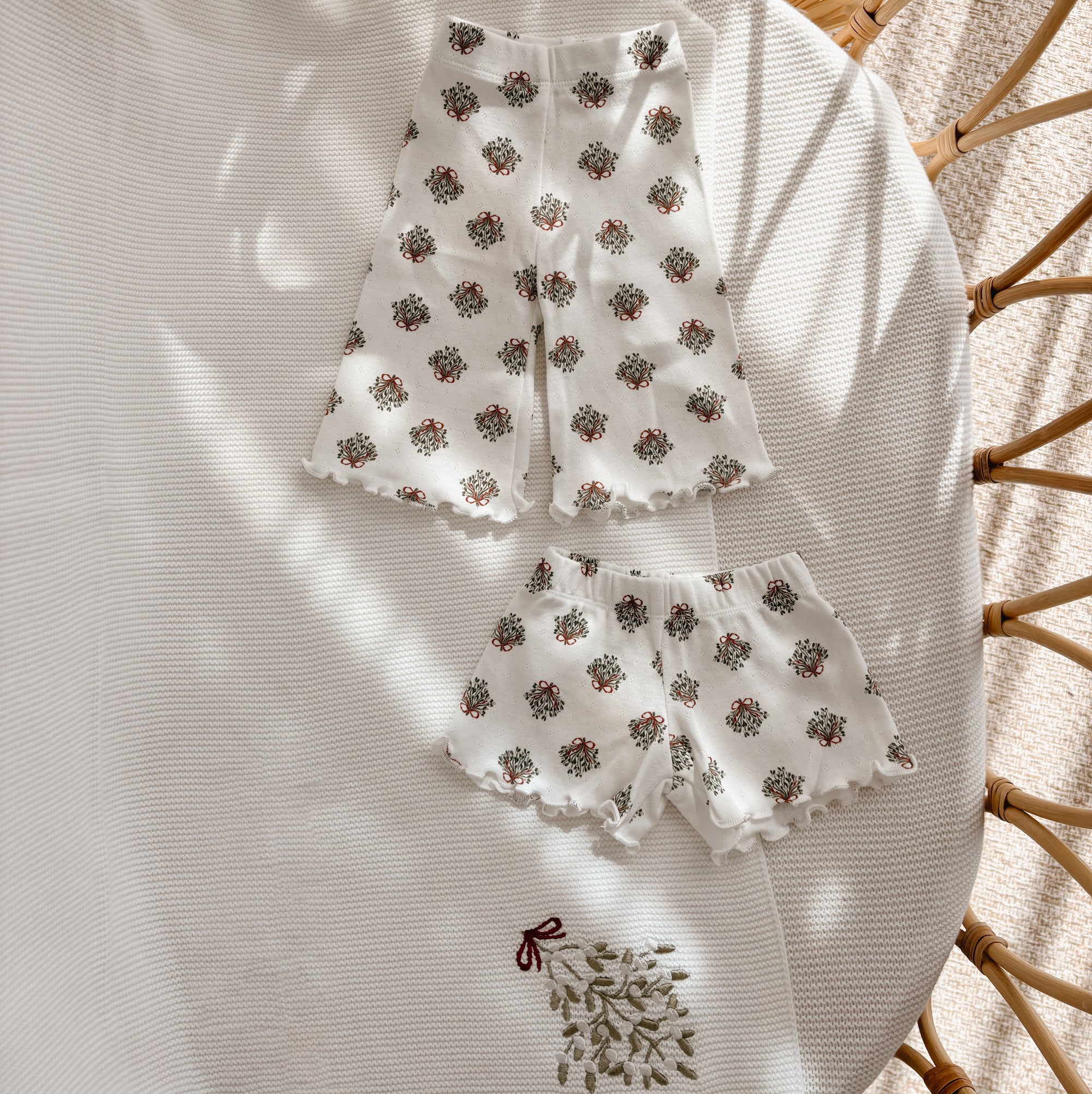 Wreath print baby flared pants and shorts with lettuce edge hems, flat lay in a bassinet