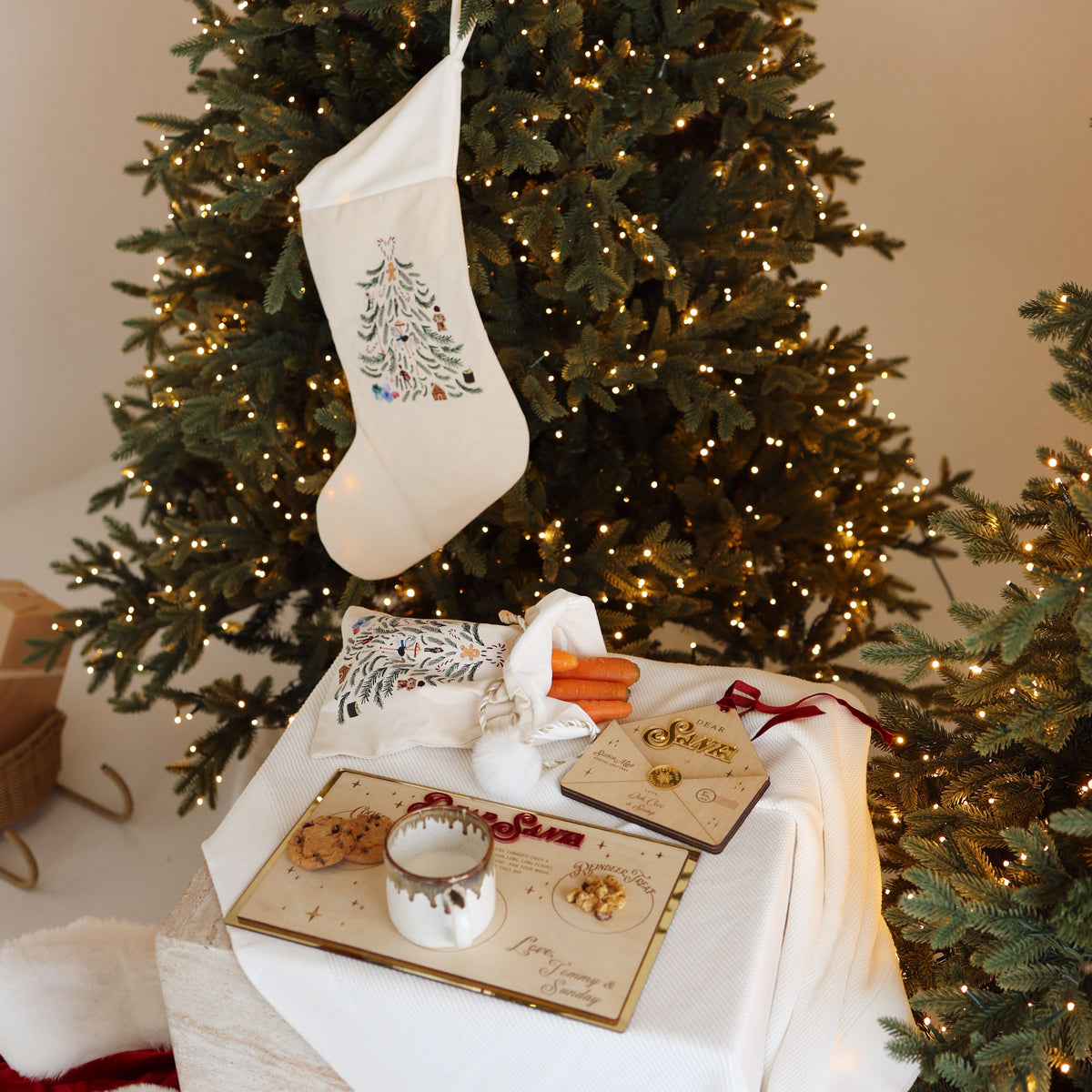 Linen Christmas stocking hanging on a Christmas tree above a mini linen Santa sack filled with carrots and a plate of treats for Santa