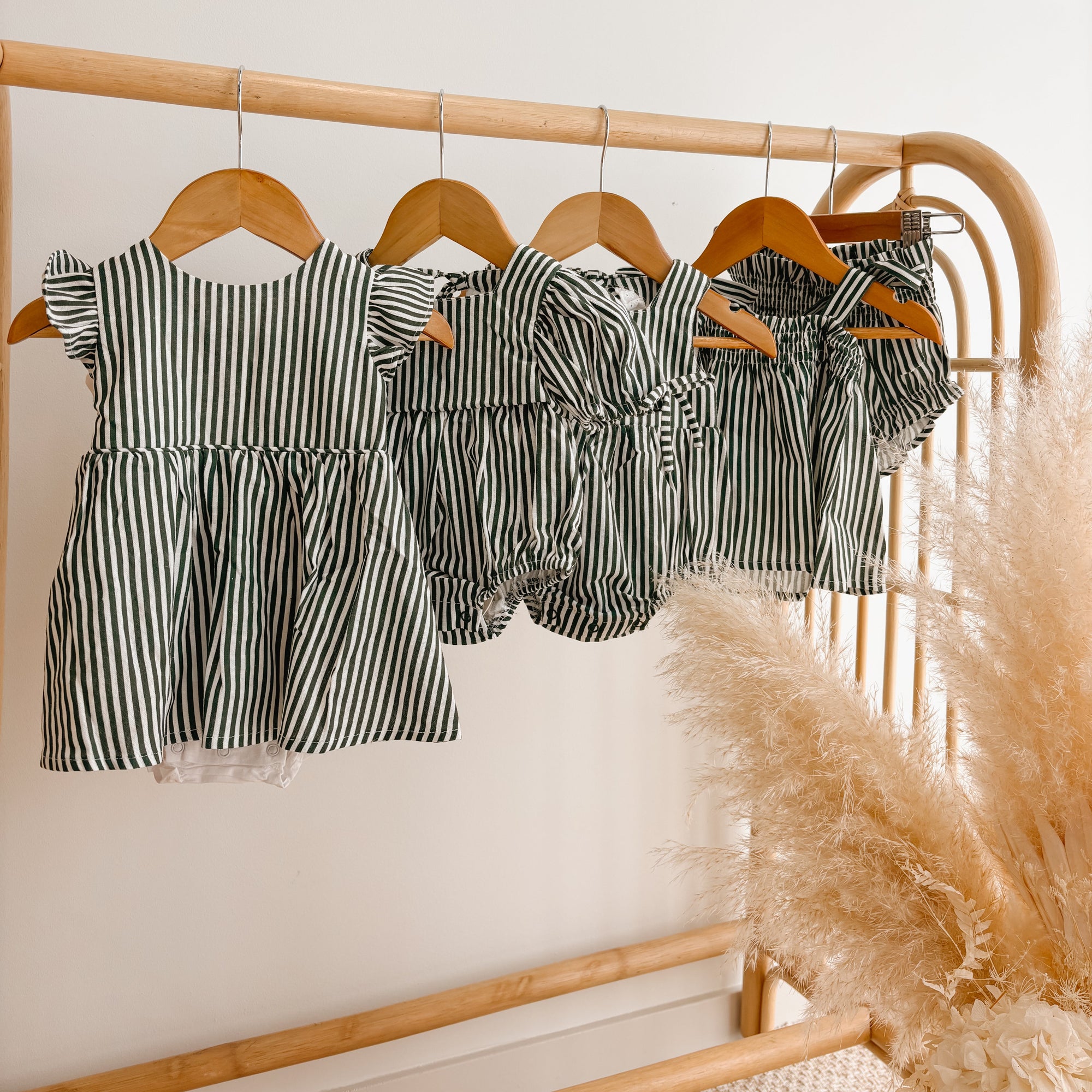Green stripe Christmas dress, romper and bloomer sets hanging together on a rattan rail