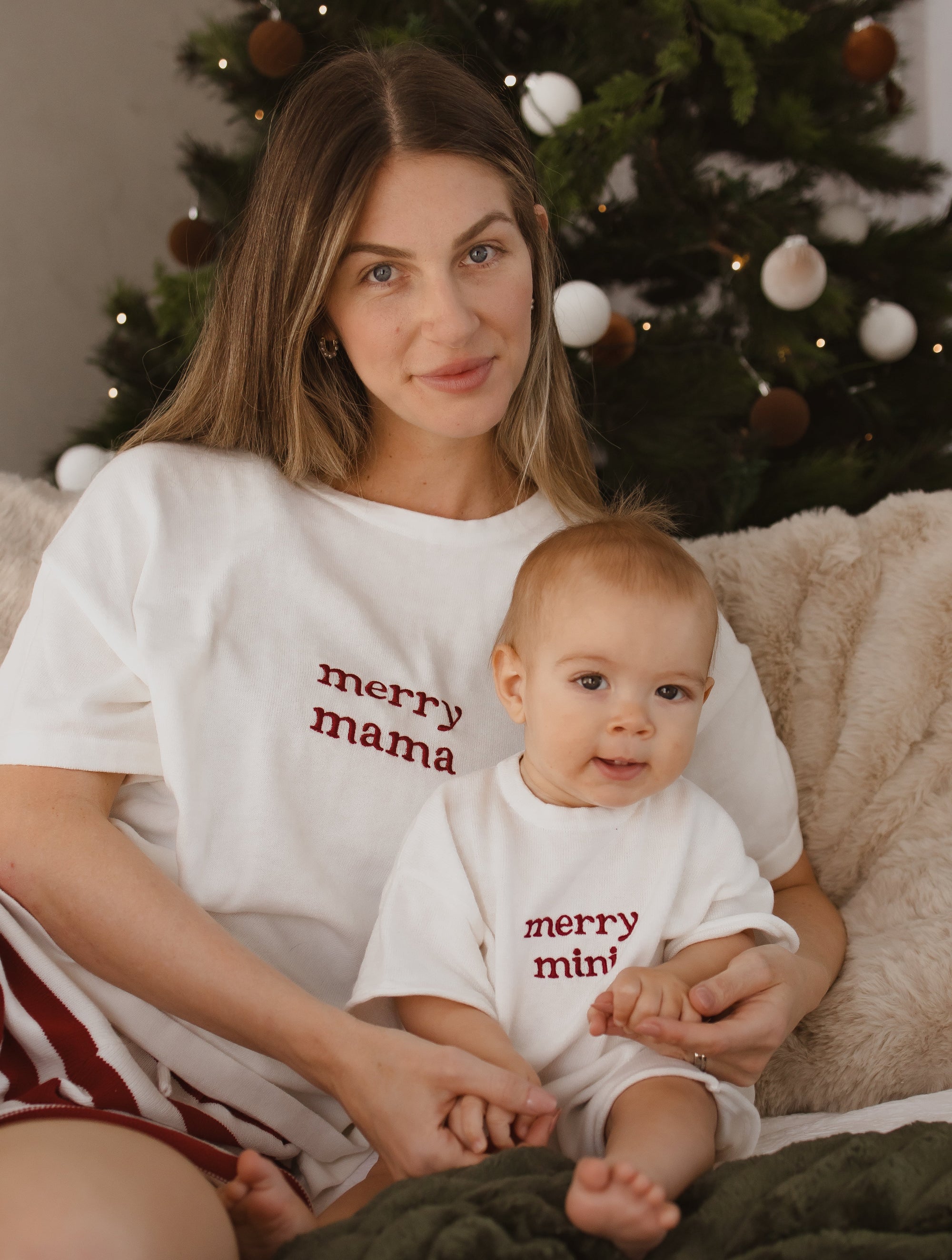 Mum and baby in matching merry mama and merry mini embroidered tees in front of a Christmas tree