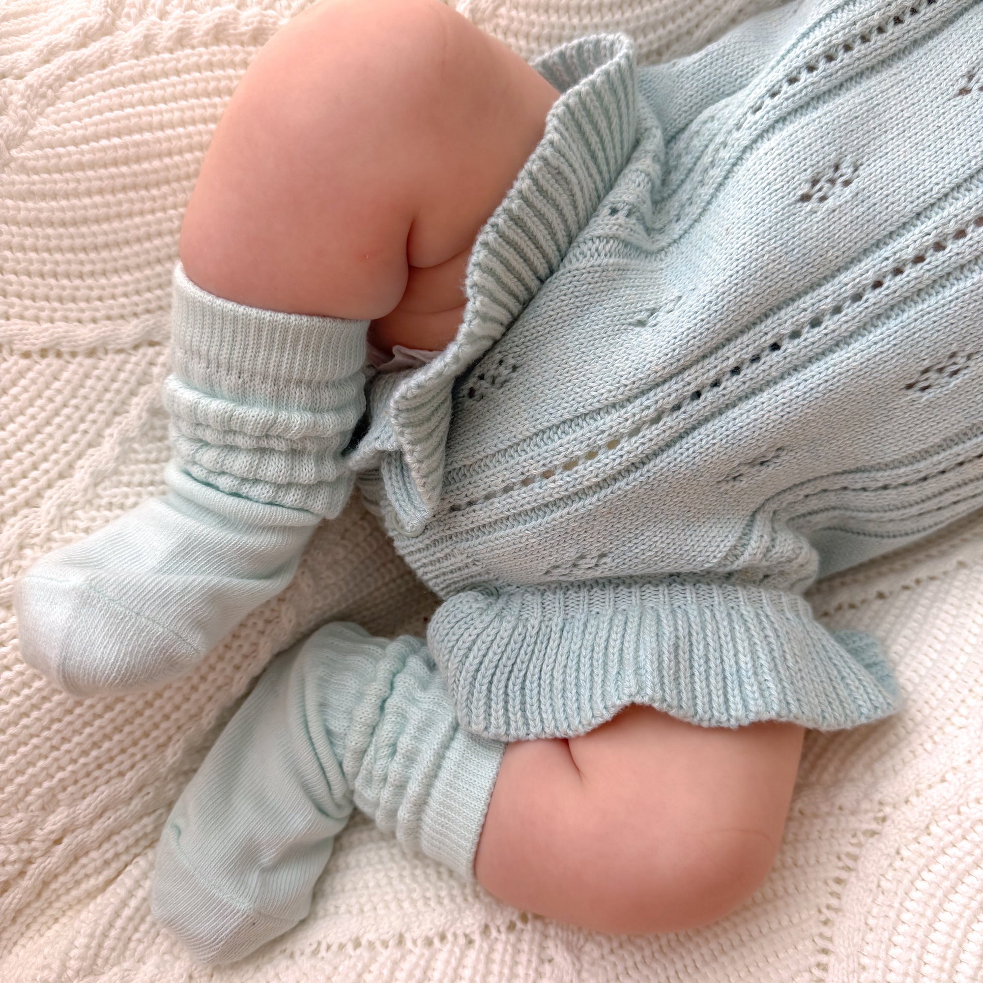 Close up of a baby in a pale blue pointelle knit romper with matching knee high socks