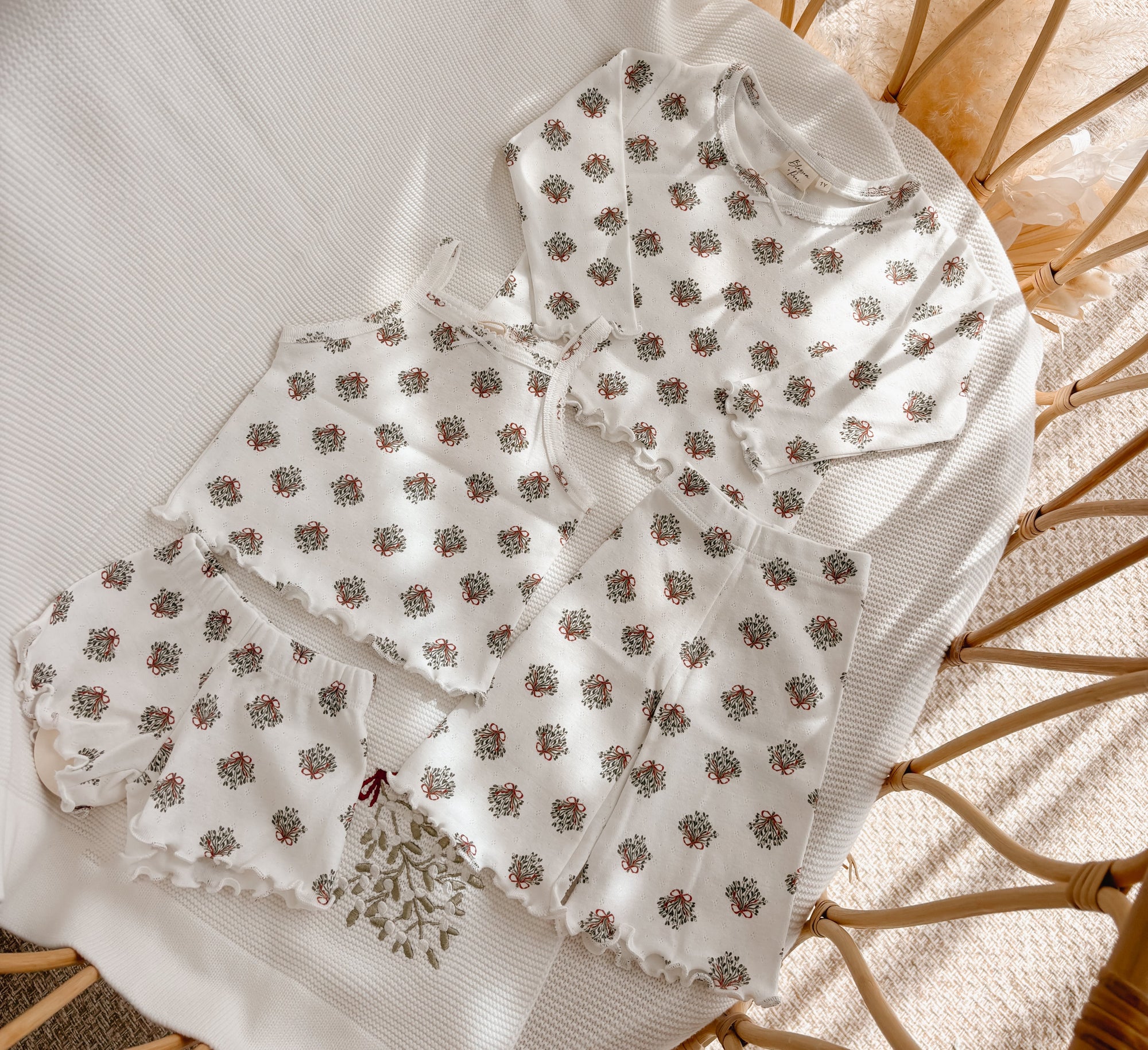 Wreath print baby top, shorts and flared pants with lettuce edge trim, flat lay in a bassinet