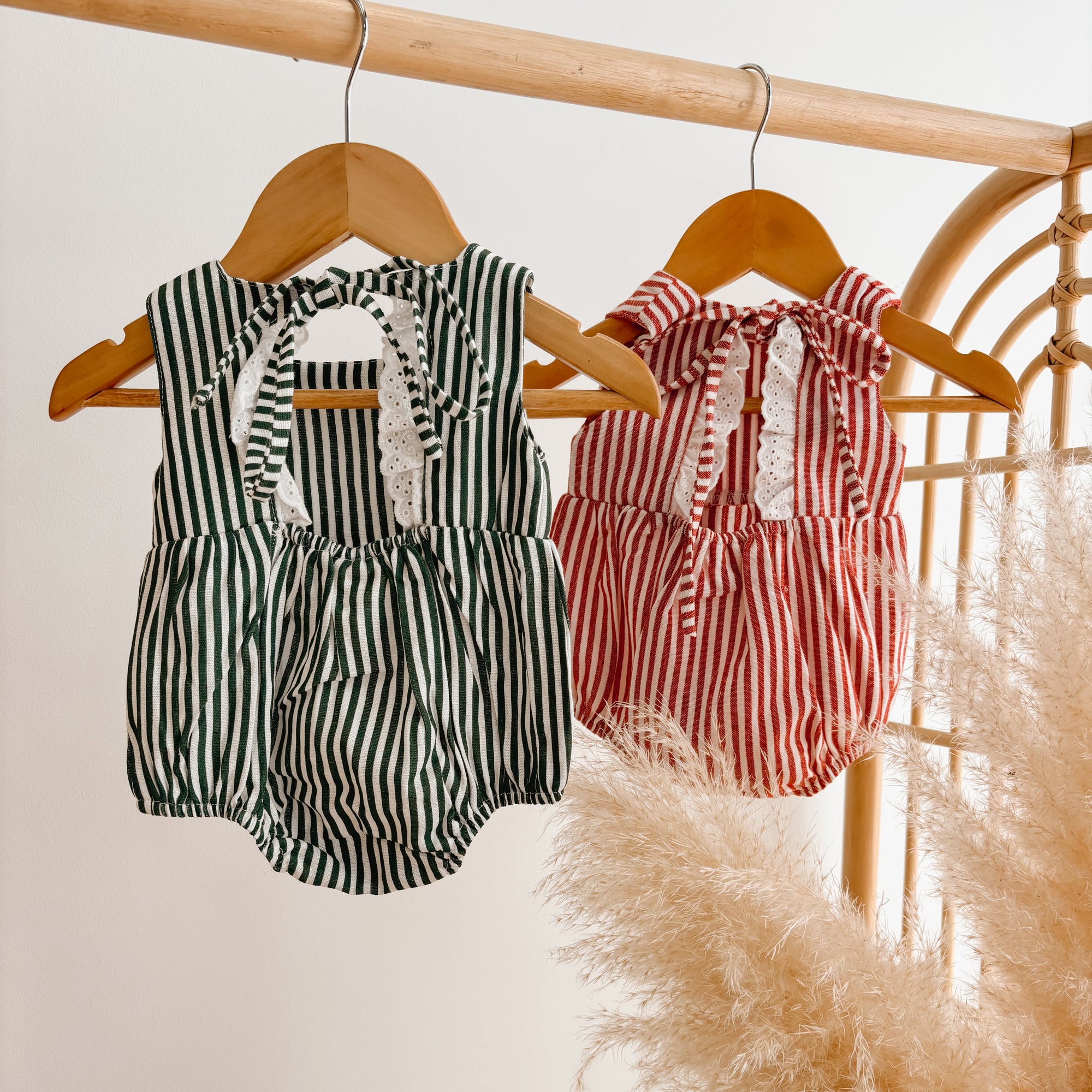 Back view of green stripe and red stripe baby rompers with tie shoulders and broderie trim