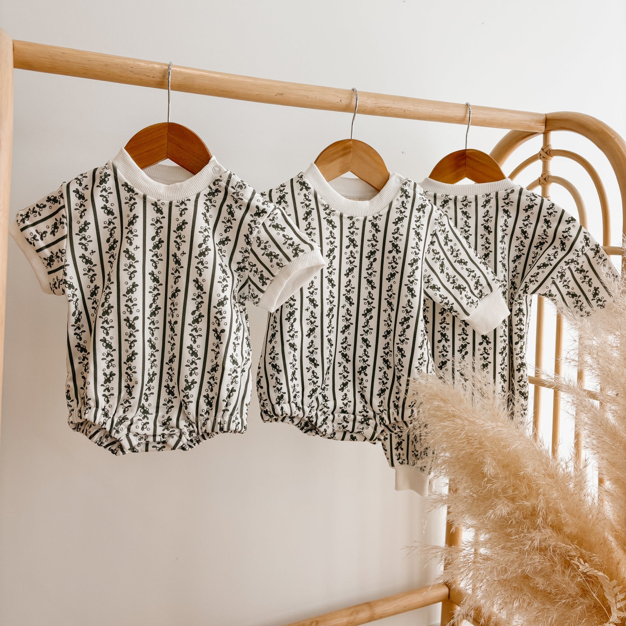 Three botanical stripe knit baby rompers in short and long sleeve styles hanging on a rattan rail