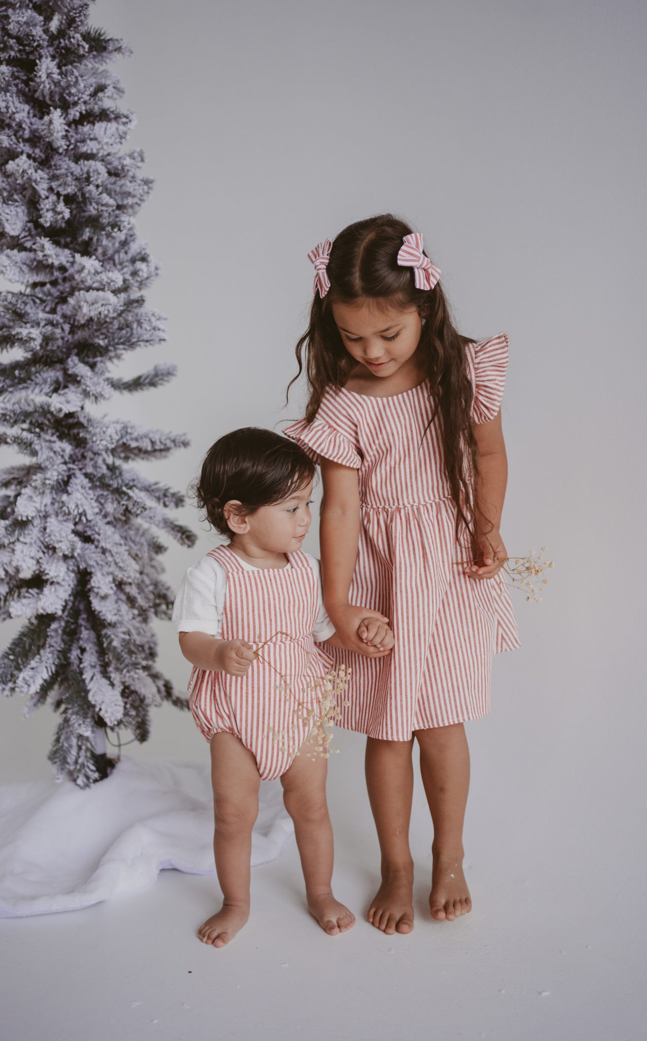 Two children in red stripe Christmas outfits, one in a flutter sleeve dress with matching hair bows