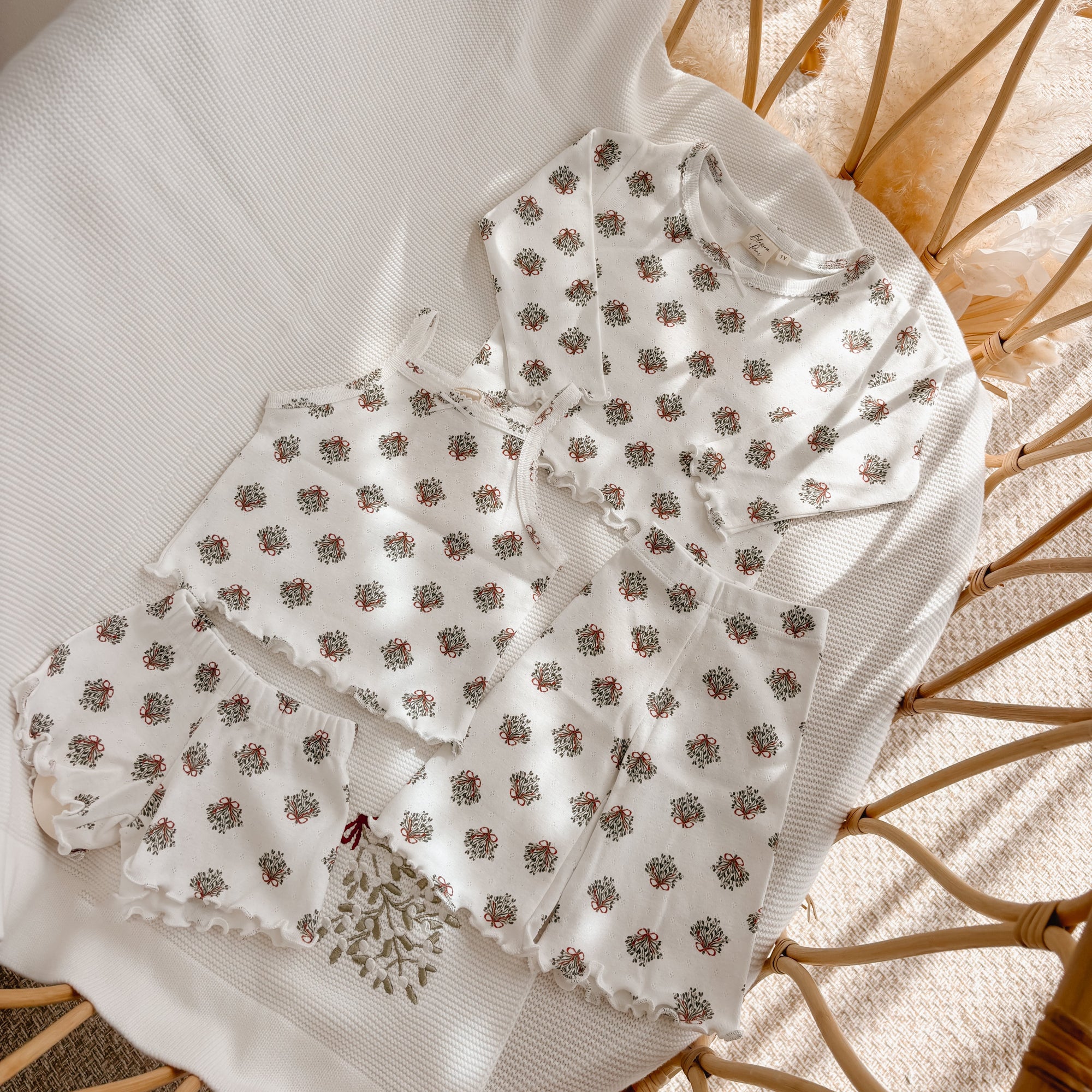 Wreath print baby top with shorts and flared pants laid out together in a bassinet