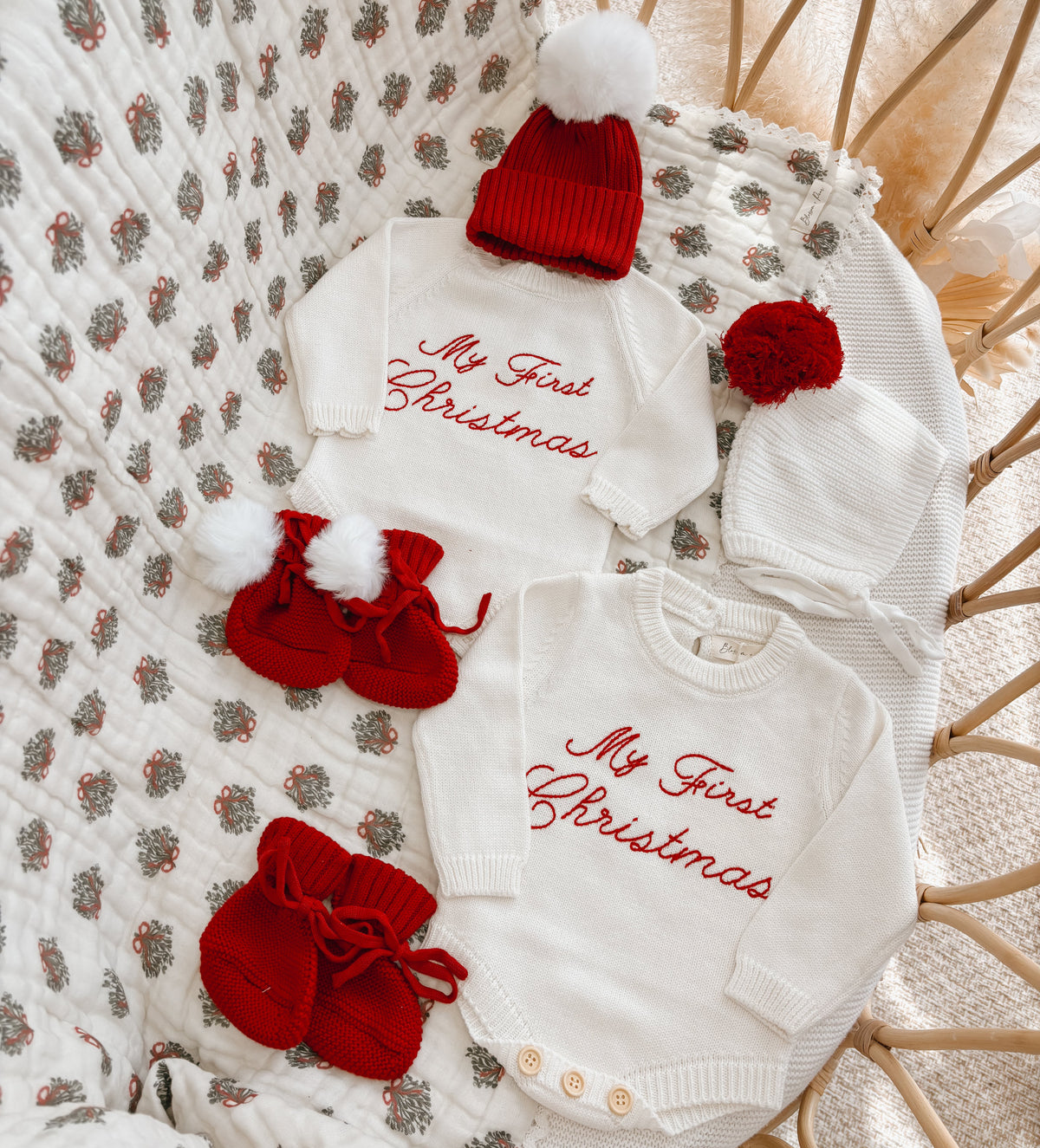 My First Christmas embroidered knit romper and jumper flat lay with red pom beanies and booties