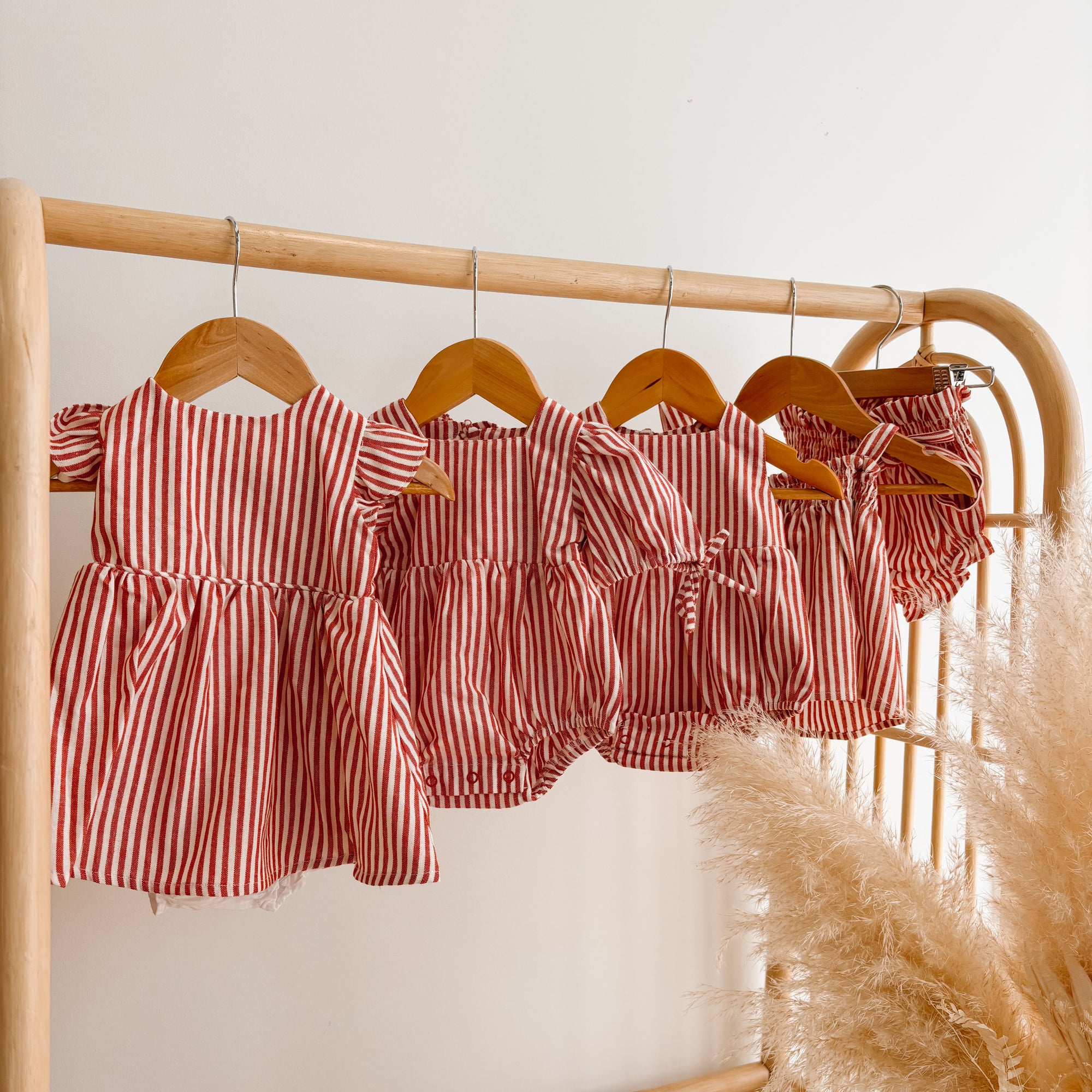 Red stripe Christmas dresses, rompers and bloomer sets hanging on a rattan clothes rail