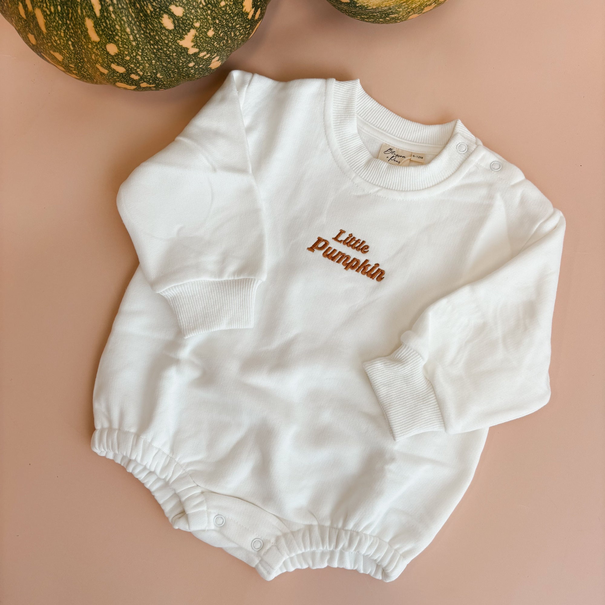 White long sleeve baby bubble romper embroidered Little Pumpkin, flat lay on pink with green pumpkins