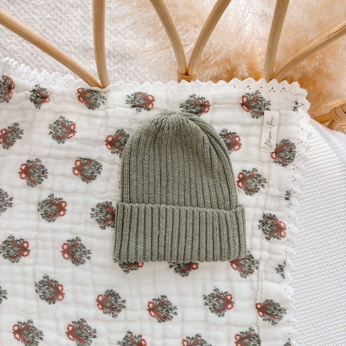 Sage green ribbed knit baby beanie on a wreath print muslin blanket in a rattan bassinet