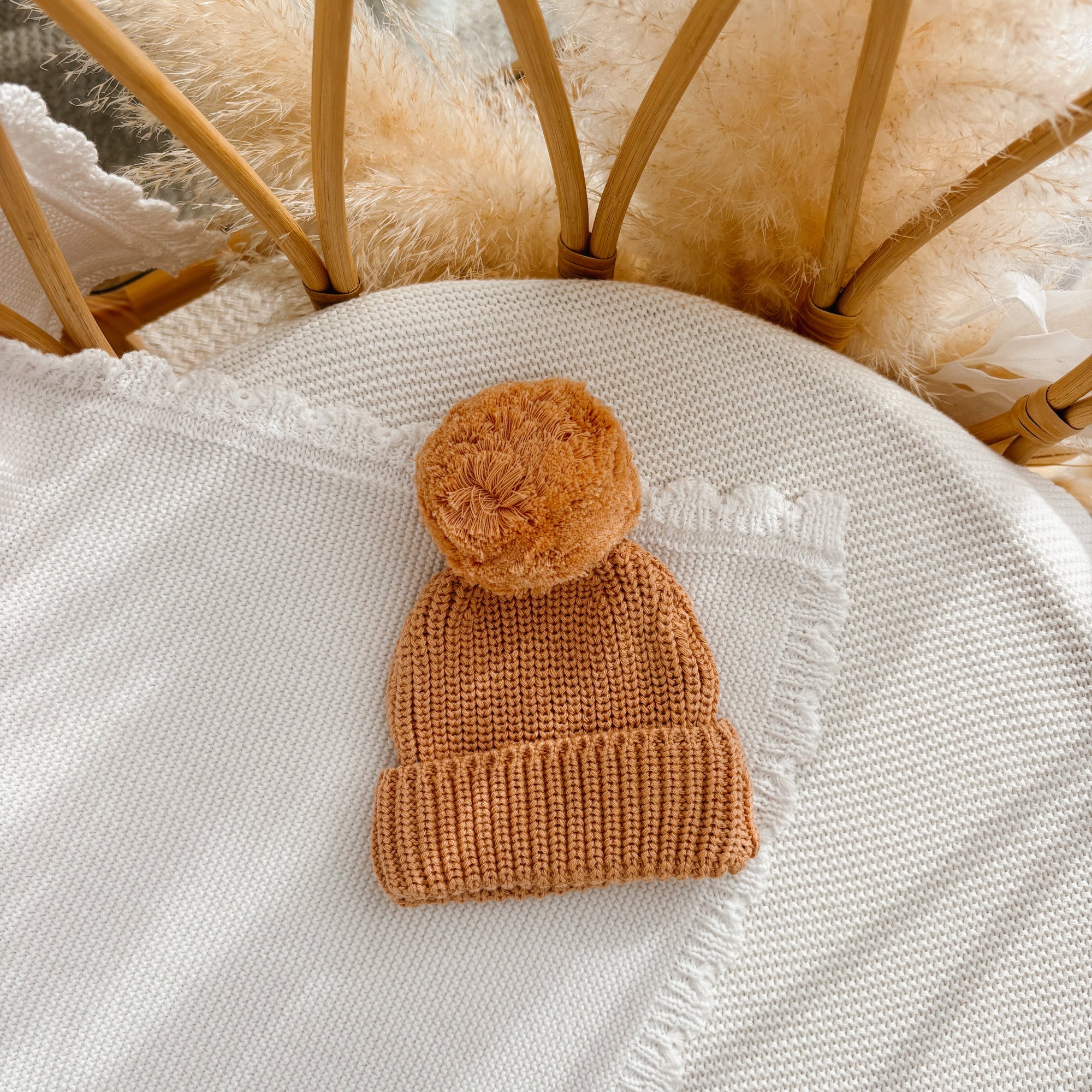 Pumpkin chunky knit baby pom beanie on a cream knit blanket