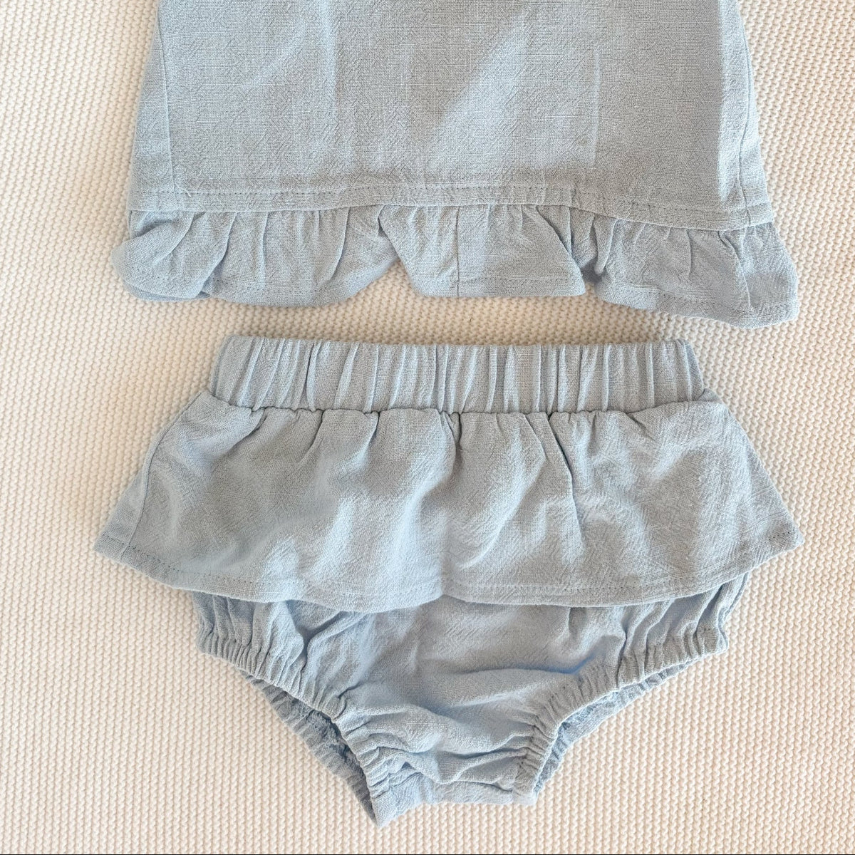 Light blue children's sleeveless top and bloomers set on a textured surface.