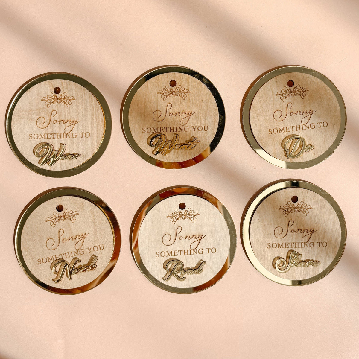 Six oval gift tags with gold borders and a small hanging hole, printed with the phrase 'Sassy Something to Do,' arranged on a peach surface with soft diagonal shadows. A kraft gift box with a white ribbon appears in the upper left corner.