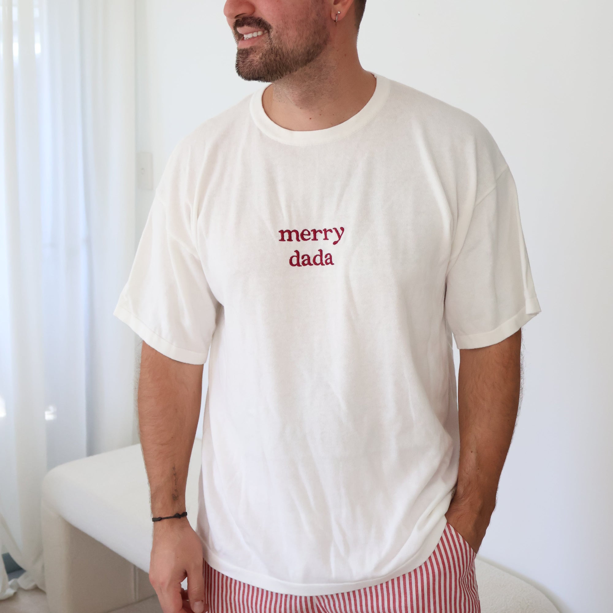 Man in a white tee embroidered with merry dada in red, worn with red stripe shorts