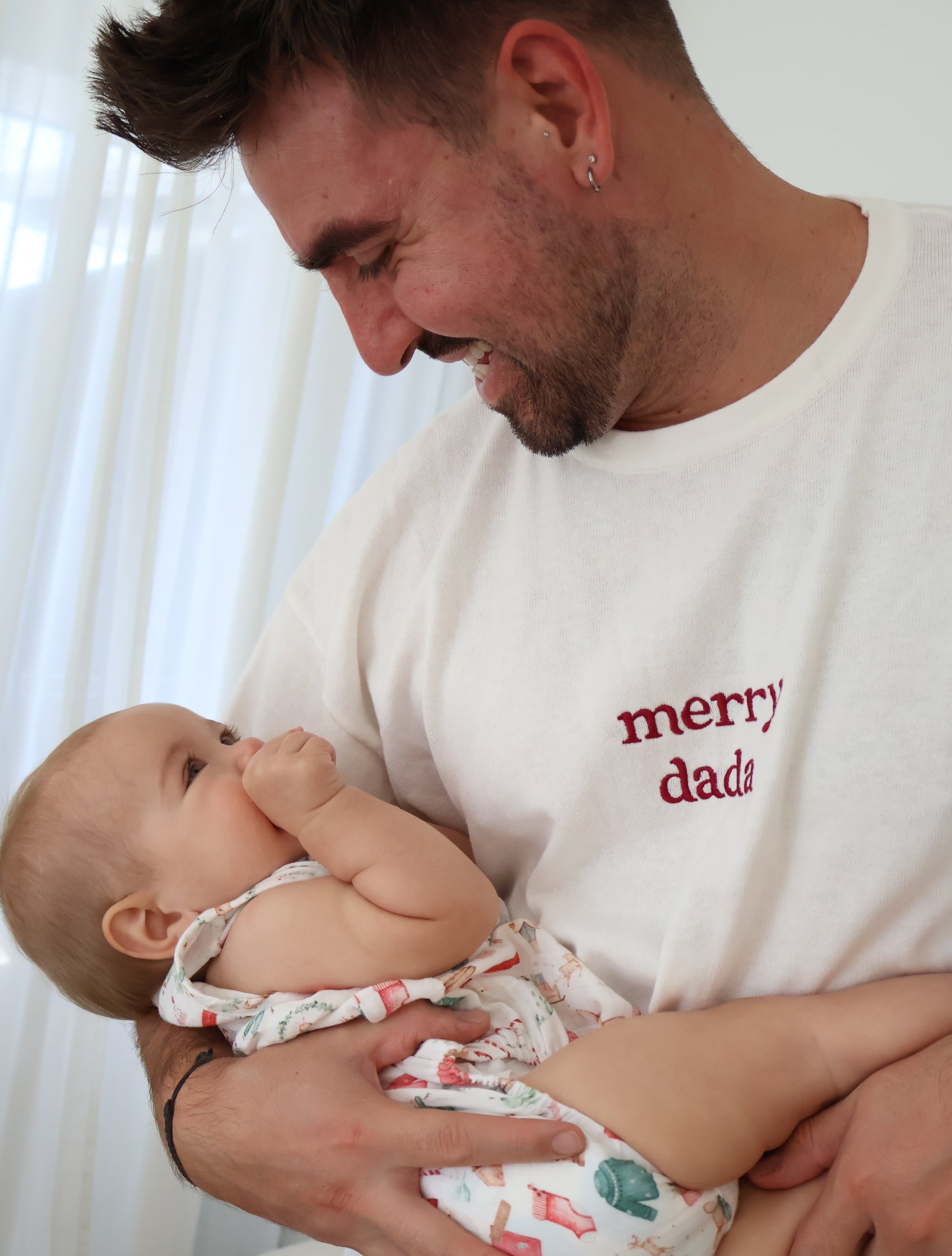 Dad in a merry dada embroidered tee smiling down at the baby in his arms