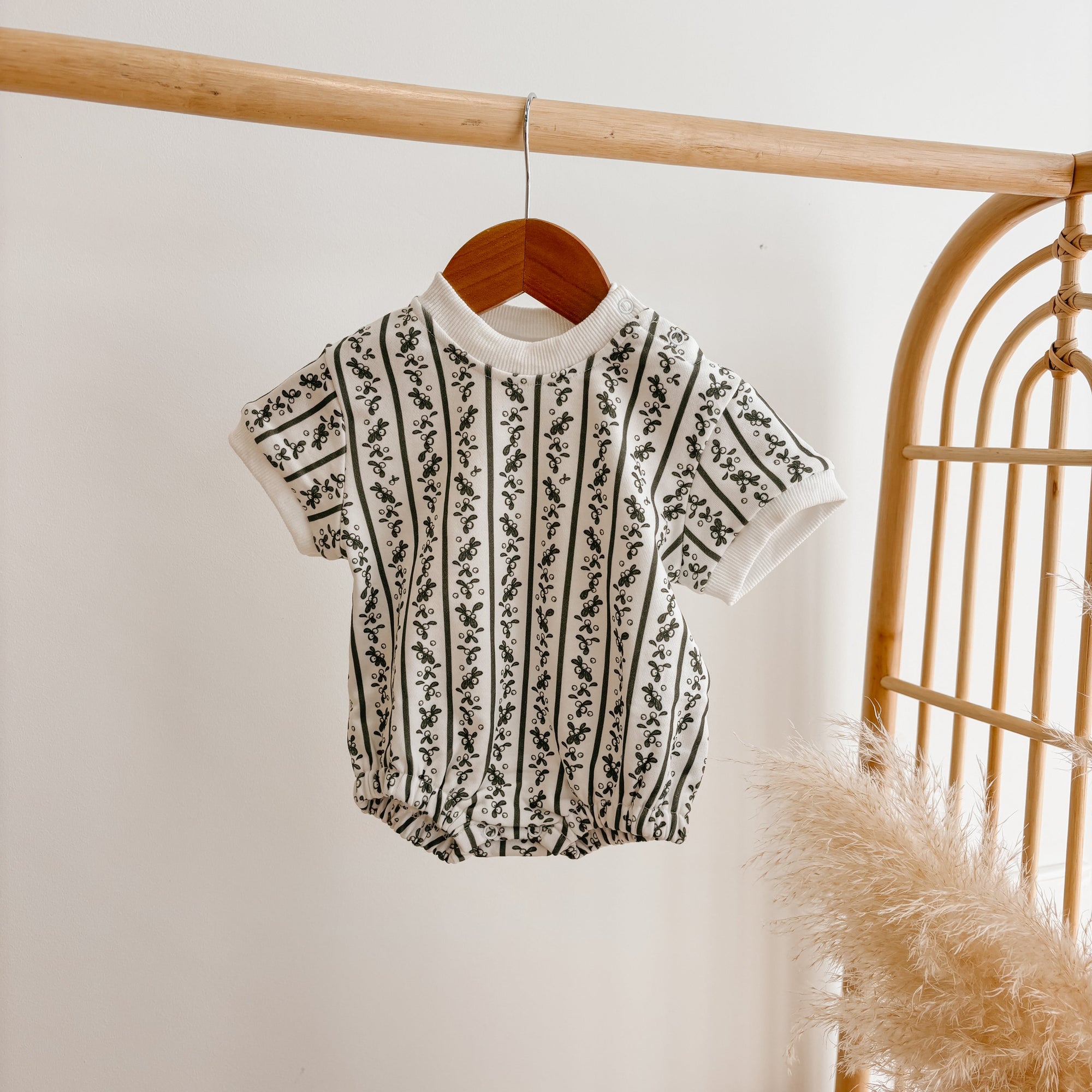 Cream knit baby romper with a black botanical stripe pattern and short sleeves, on a wooden hanger