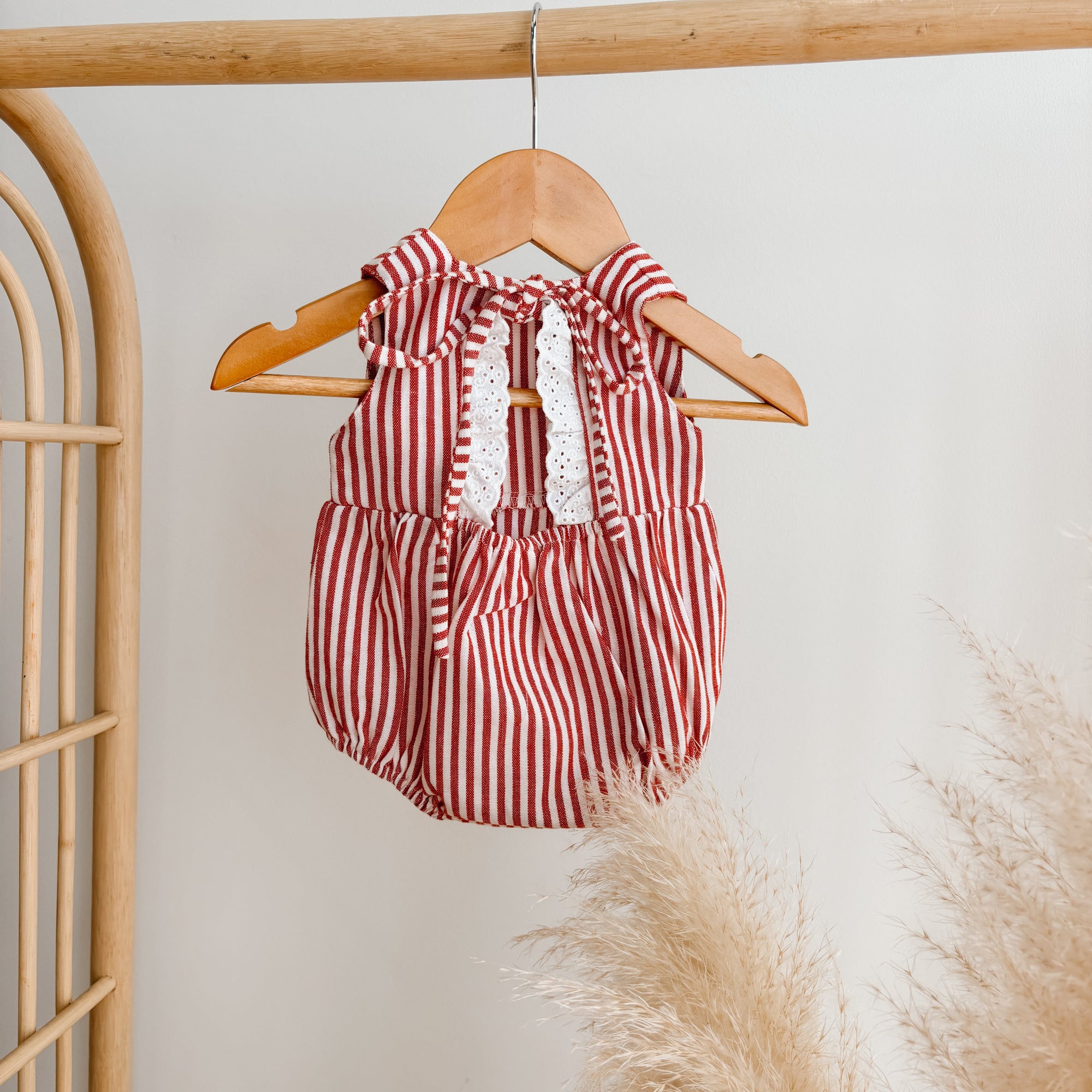 Red stripe baby romper with tie shoulder straps and broderie trim on a wooden hanger