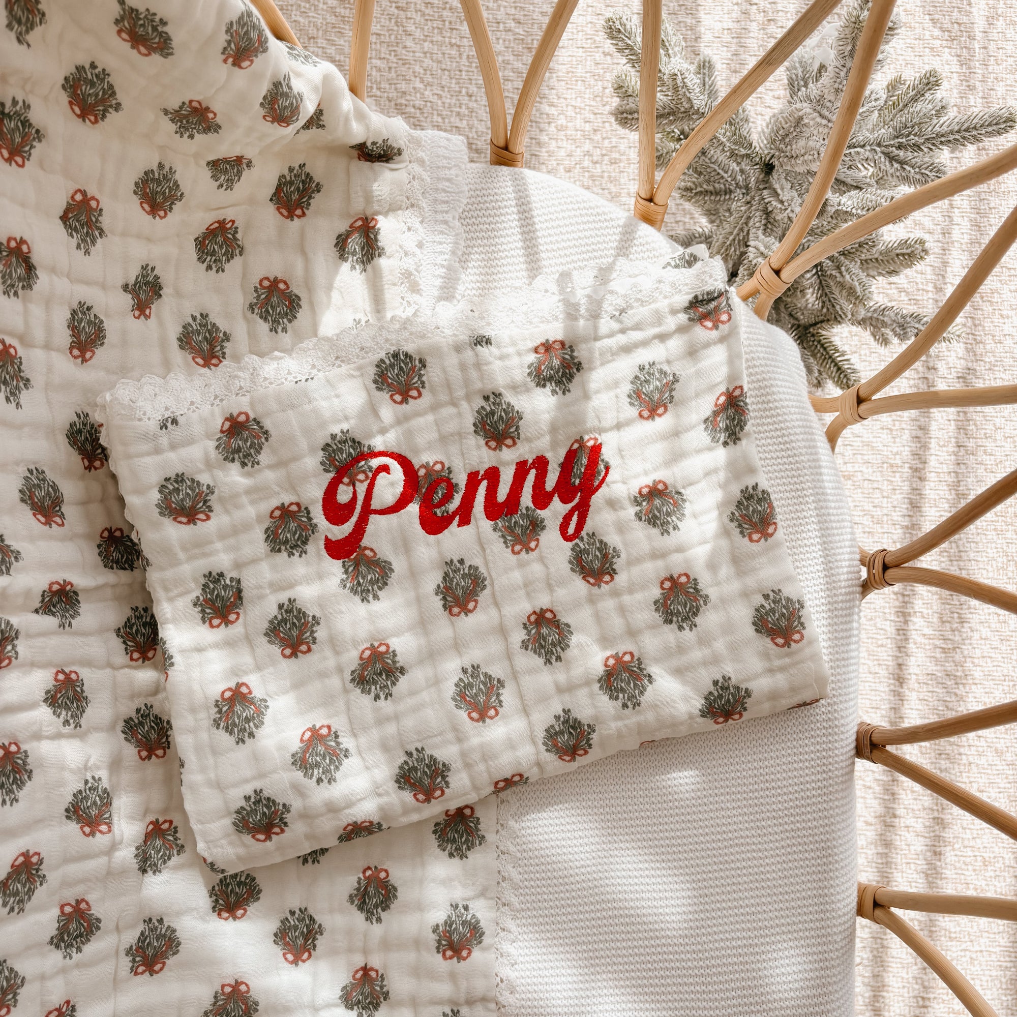 Personalised wreath print muslin baby blanket embroidered with a name in red script, in a rattan bassinet