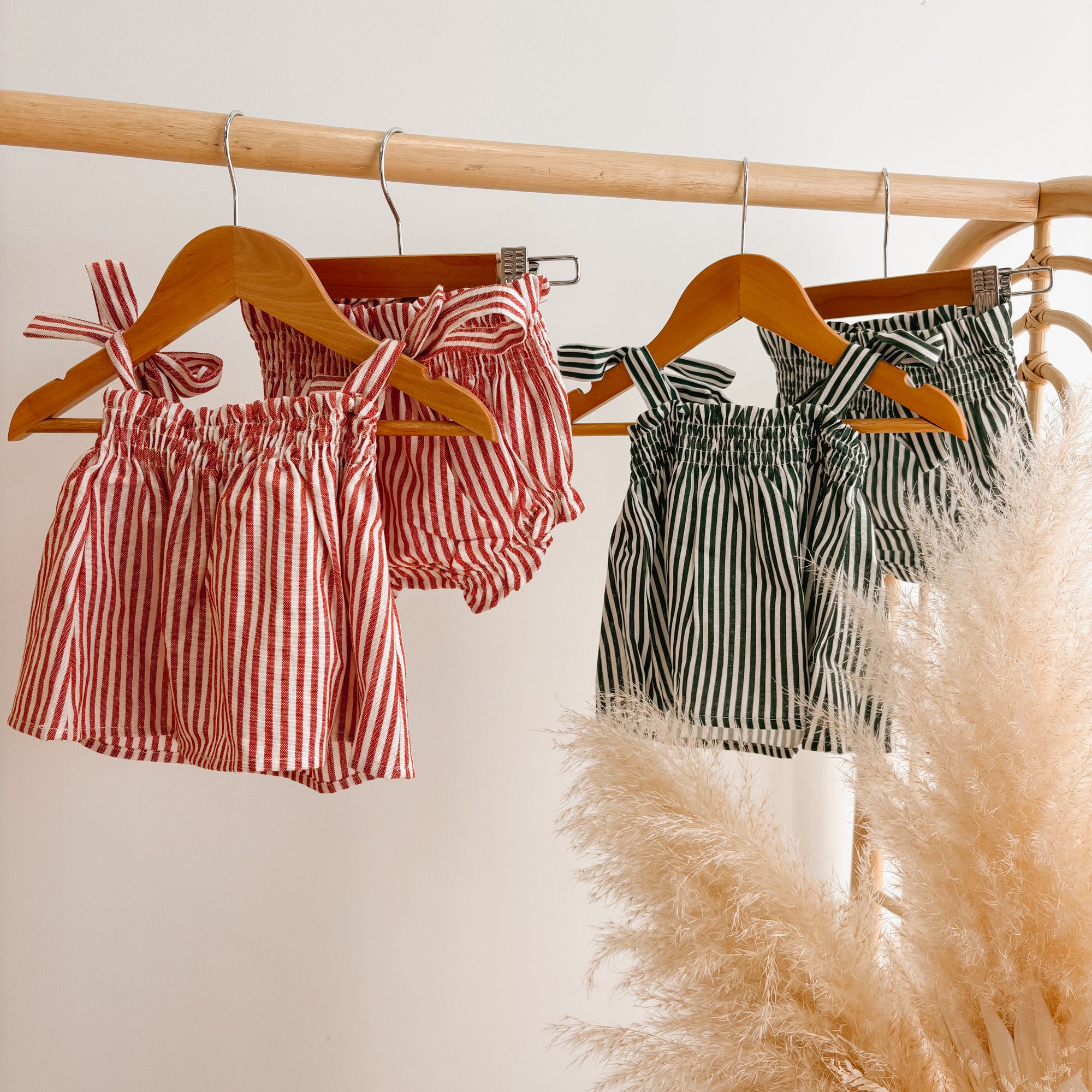 Red stripe and green stripe baby top and bloomer sets hanging on a rattan clothes rail