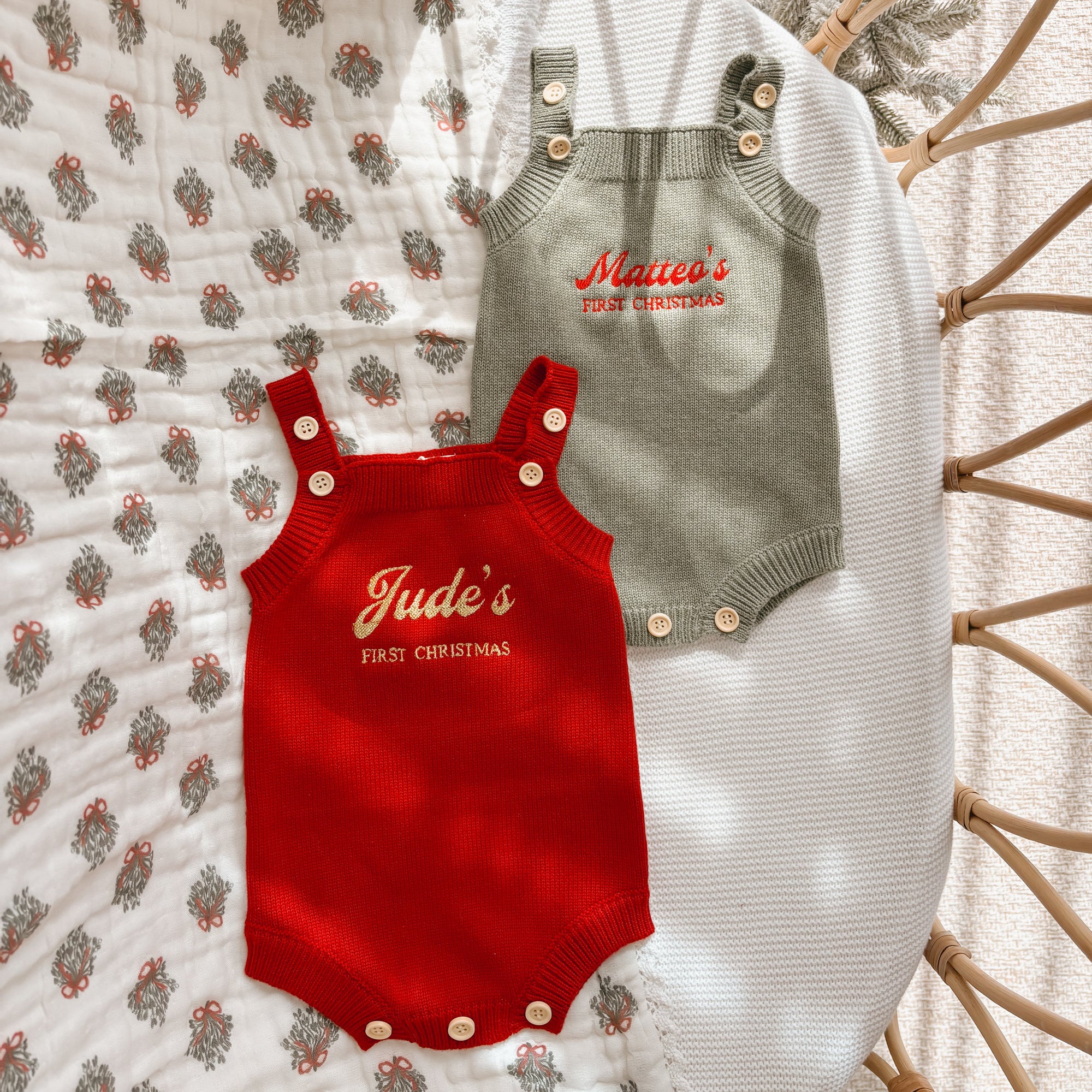 Two personalised First Christmas knit baby rompers in red and sage, embroidered with names