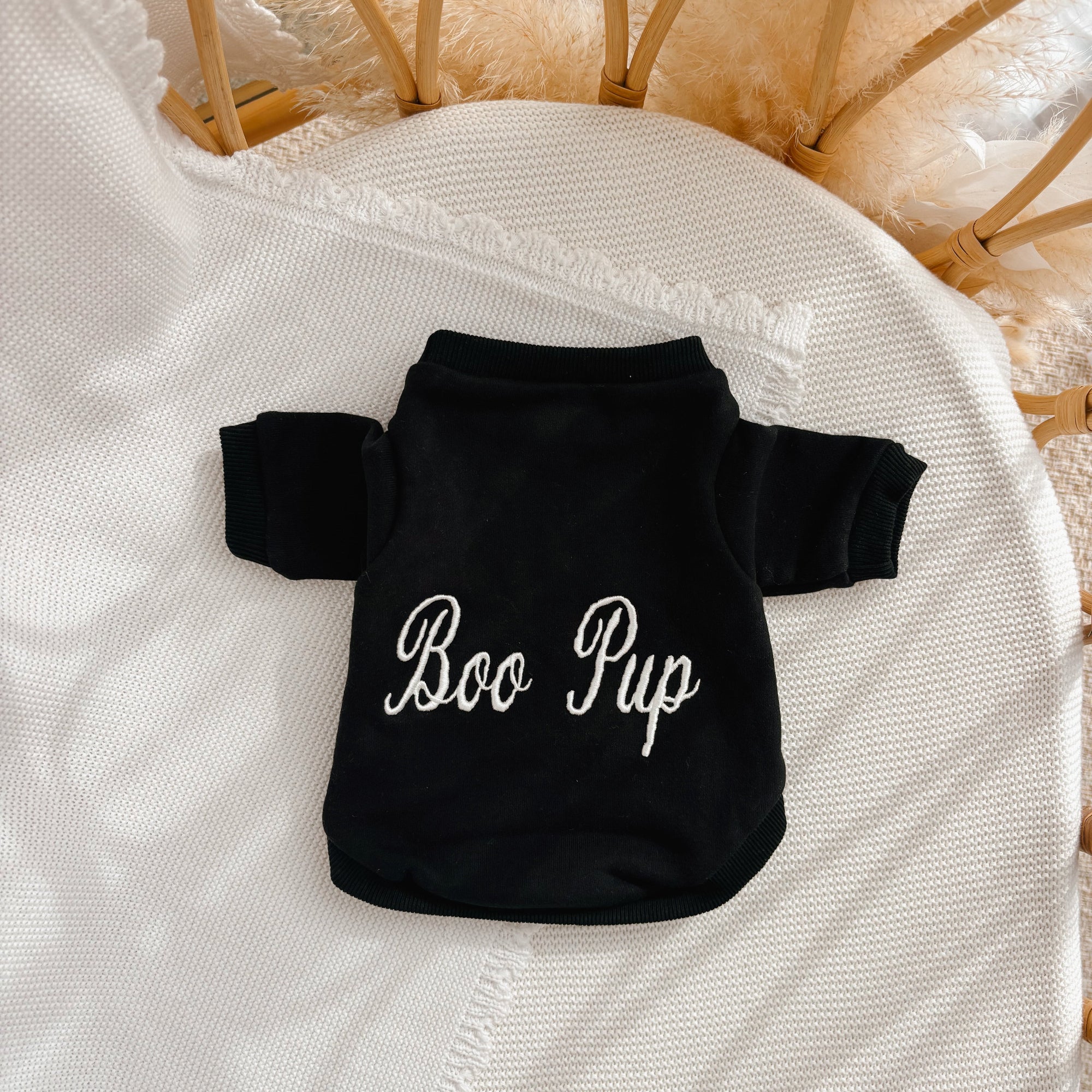Personalised black dog jumper embroidered with 'Boo Pup' in white script, flat lay on a cream knit blanket