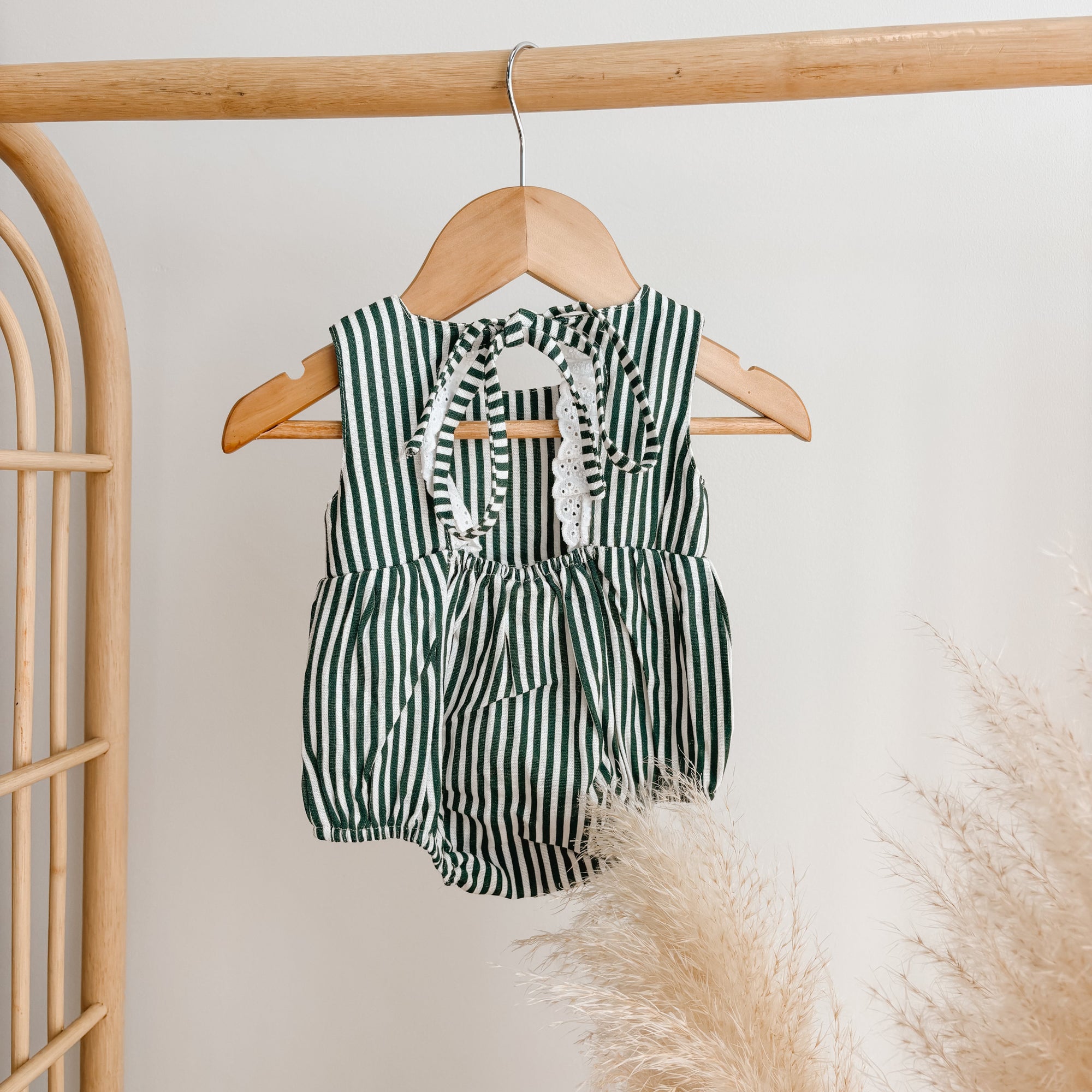 Green stripe baby romper with tie shoulder straps and broderie trim on a wooden hanger