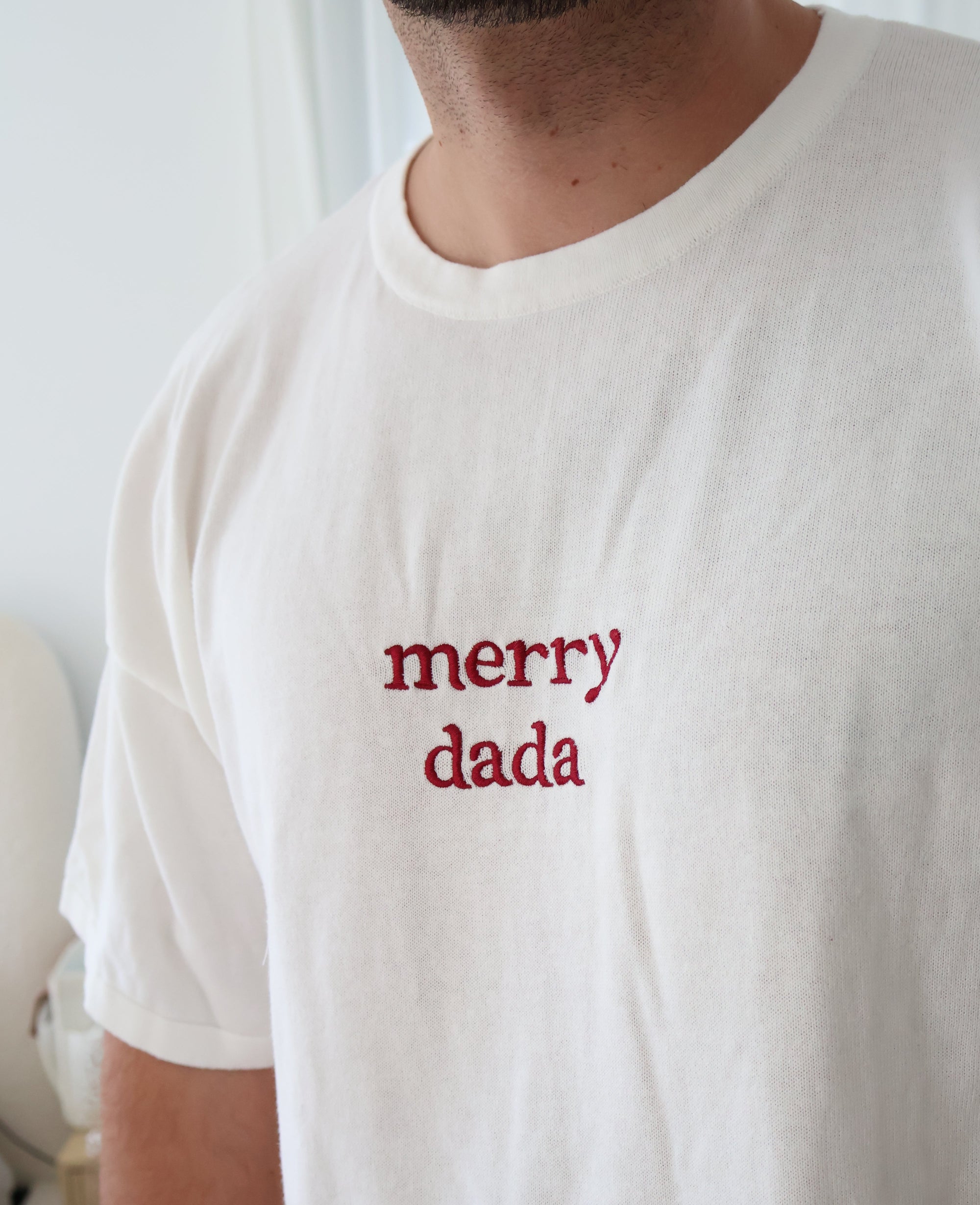 Close up of red merry dada embroidery on a white cotton tee