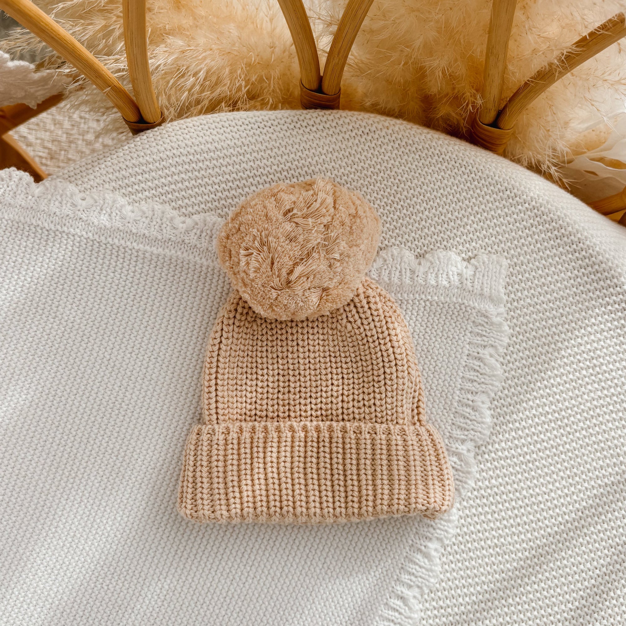 Vanilla Oat chunky knit baby pom beanie on a cream knit blanket