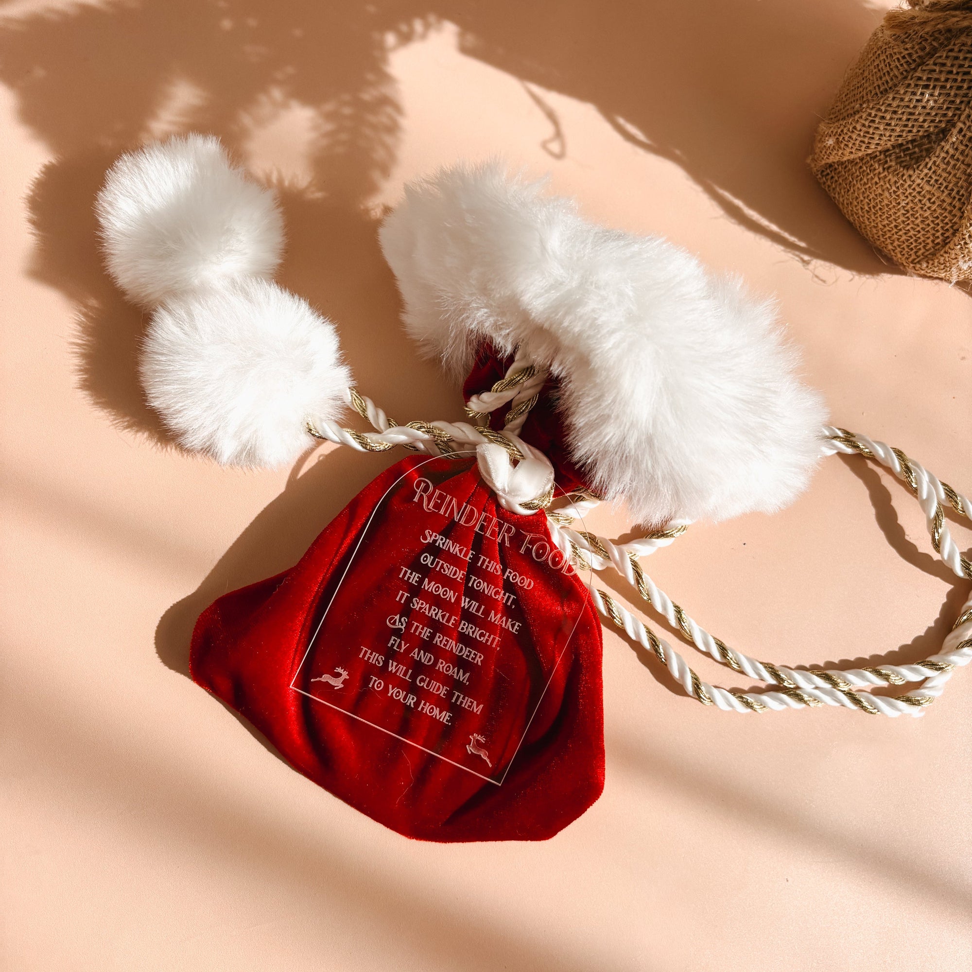 A red velvet Christmas stocking ornament featuring white faux fur trim, a white rope handle, and a hanging ornament with the text 'REINDEER FOOD' and a list of instructions.