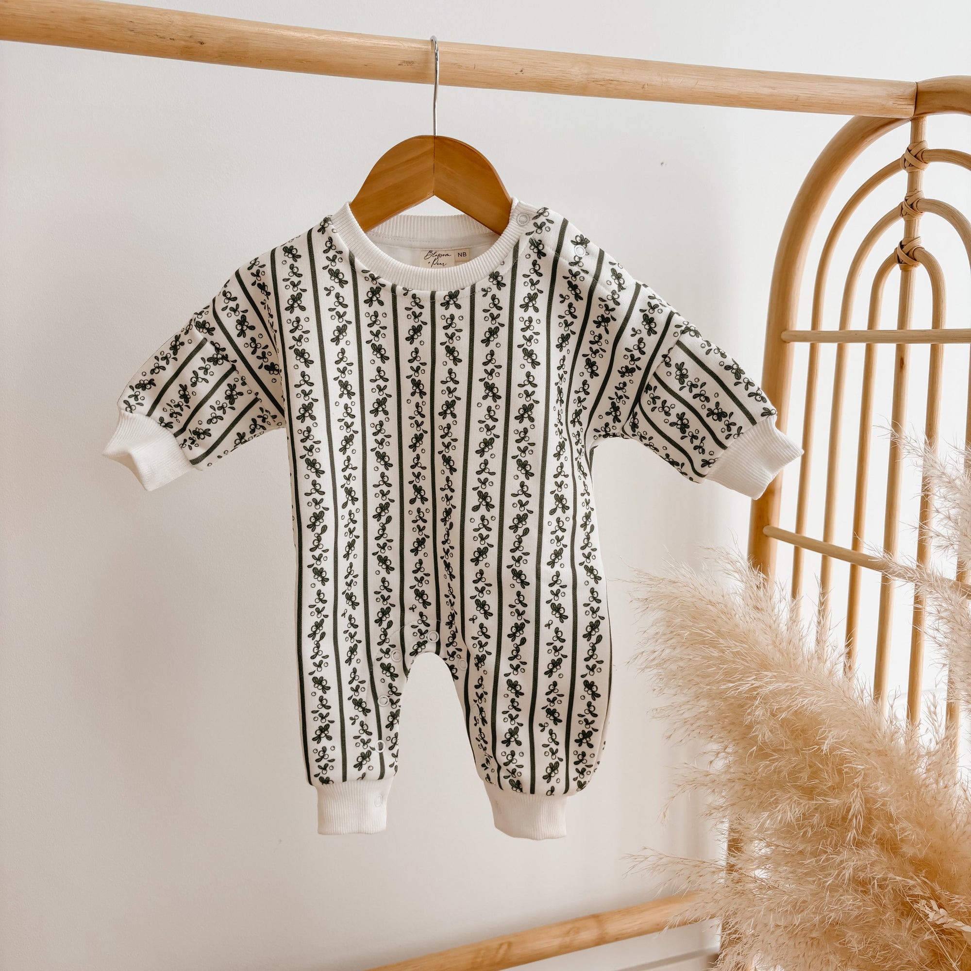 Cream knit baby jumpsuit with a black botanical stripe pattern, hanging on a wooden hanger