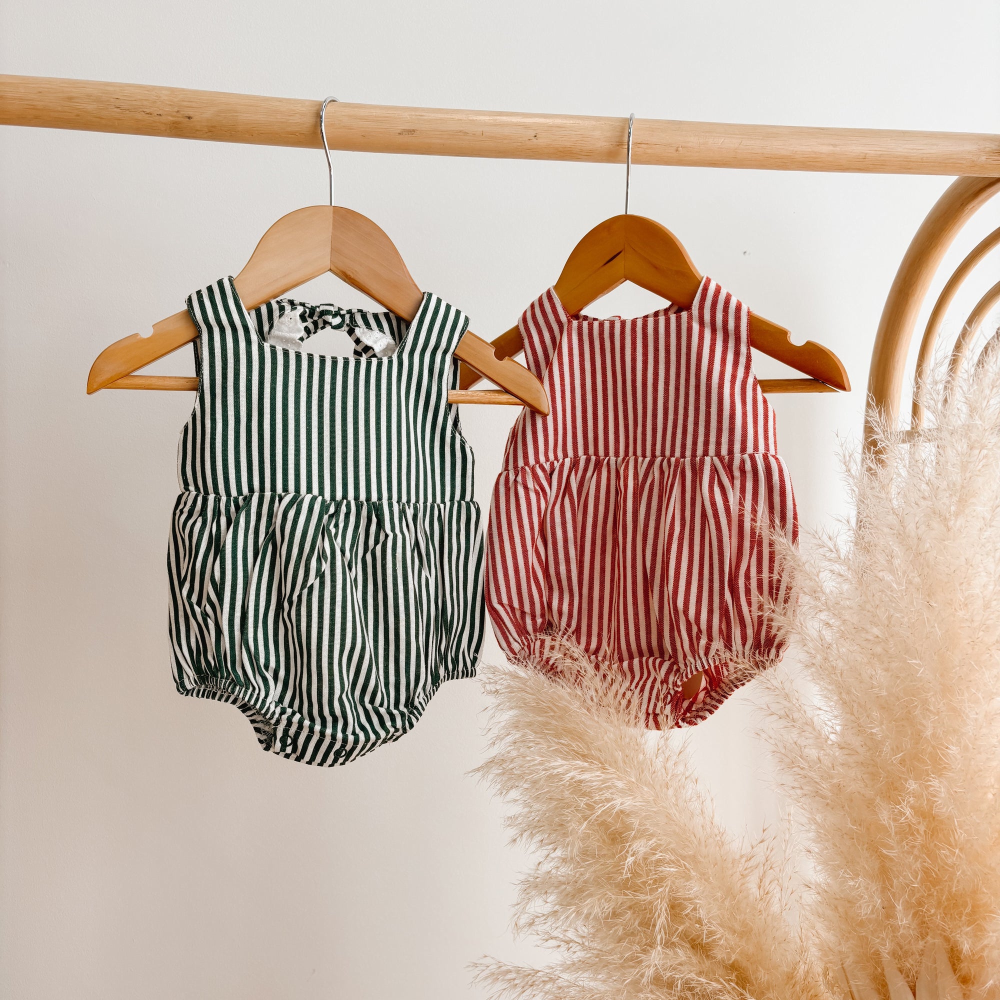 Green stripe and red stripe baby rompers hanging side by side on wooden hangers