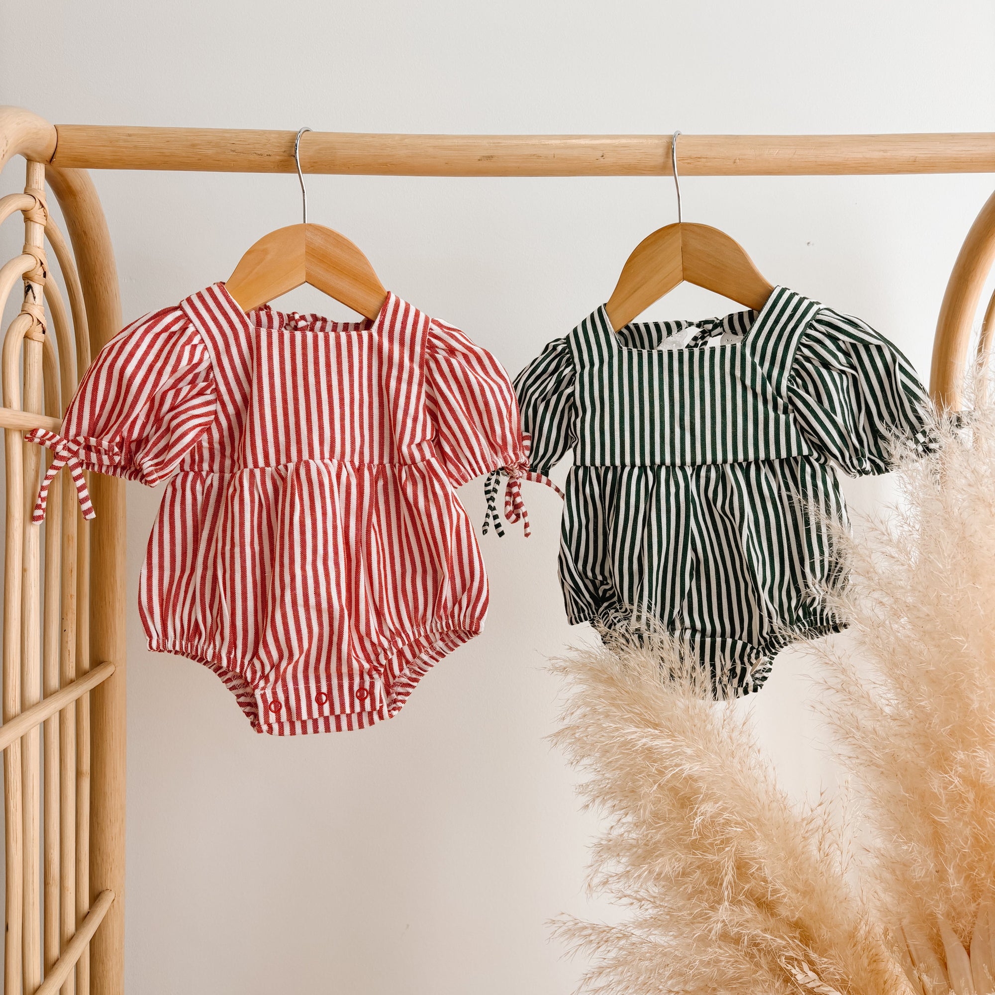 Red stripe and green stripe puff sleeve baby rompers hanging on wooden hangers