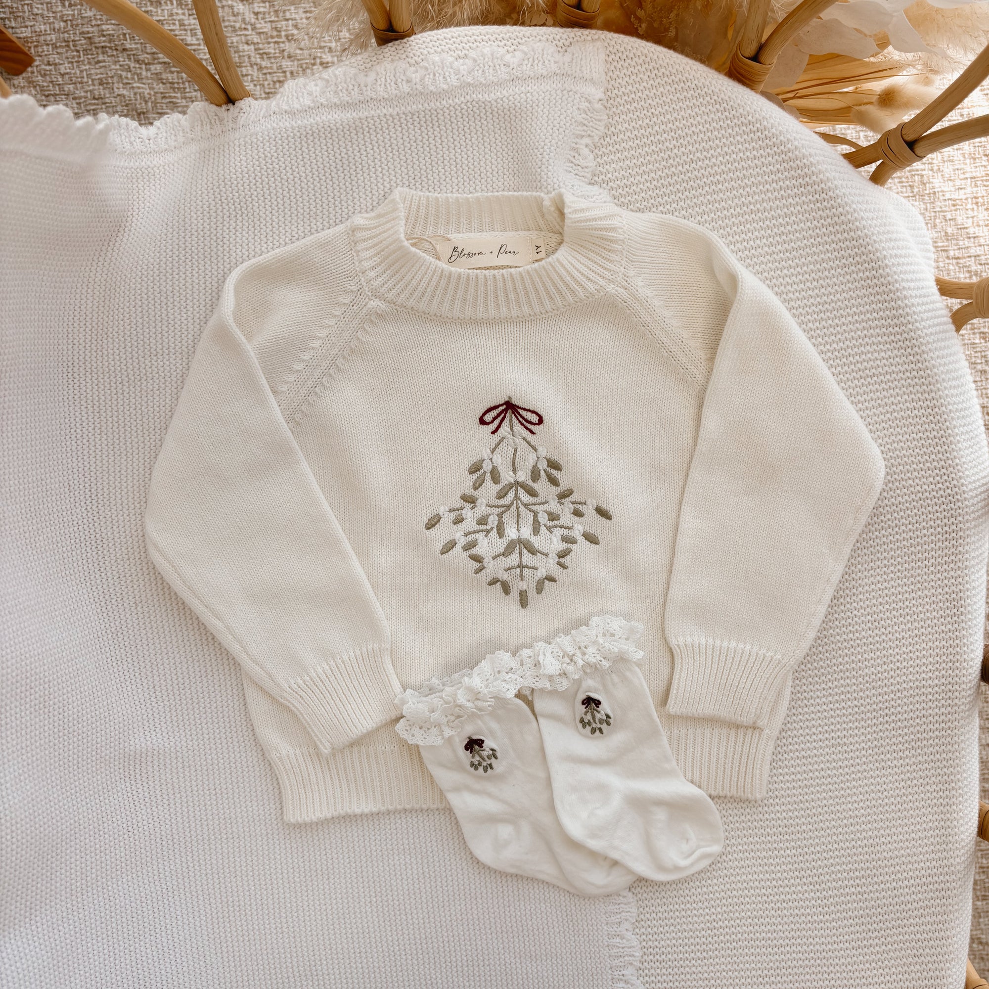 Cream knit baby jumper embroidered with mistletoe and a red bow, with matching frill socks