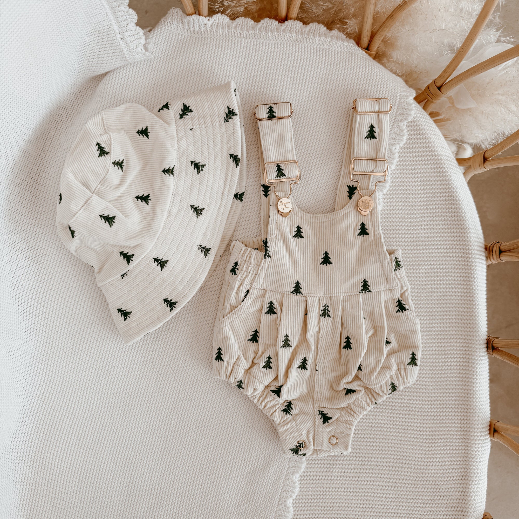 Christmas tree print corduroy baby overall romper with a matching bucket hat, flat lay in a bassinet