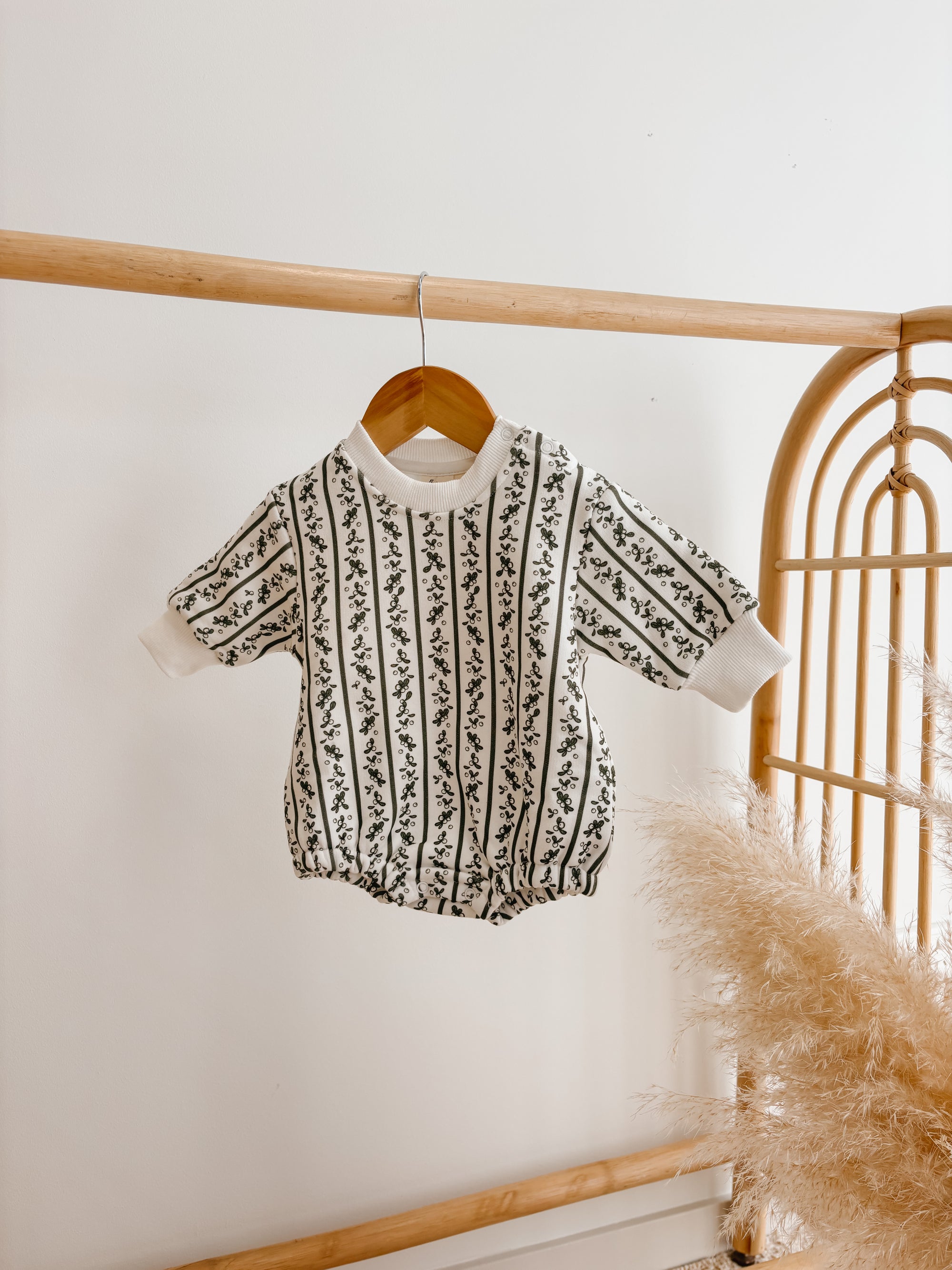 Cream long sleeve knit baby romper with a black botanical stripe pattern, hanging on a wooden hanger