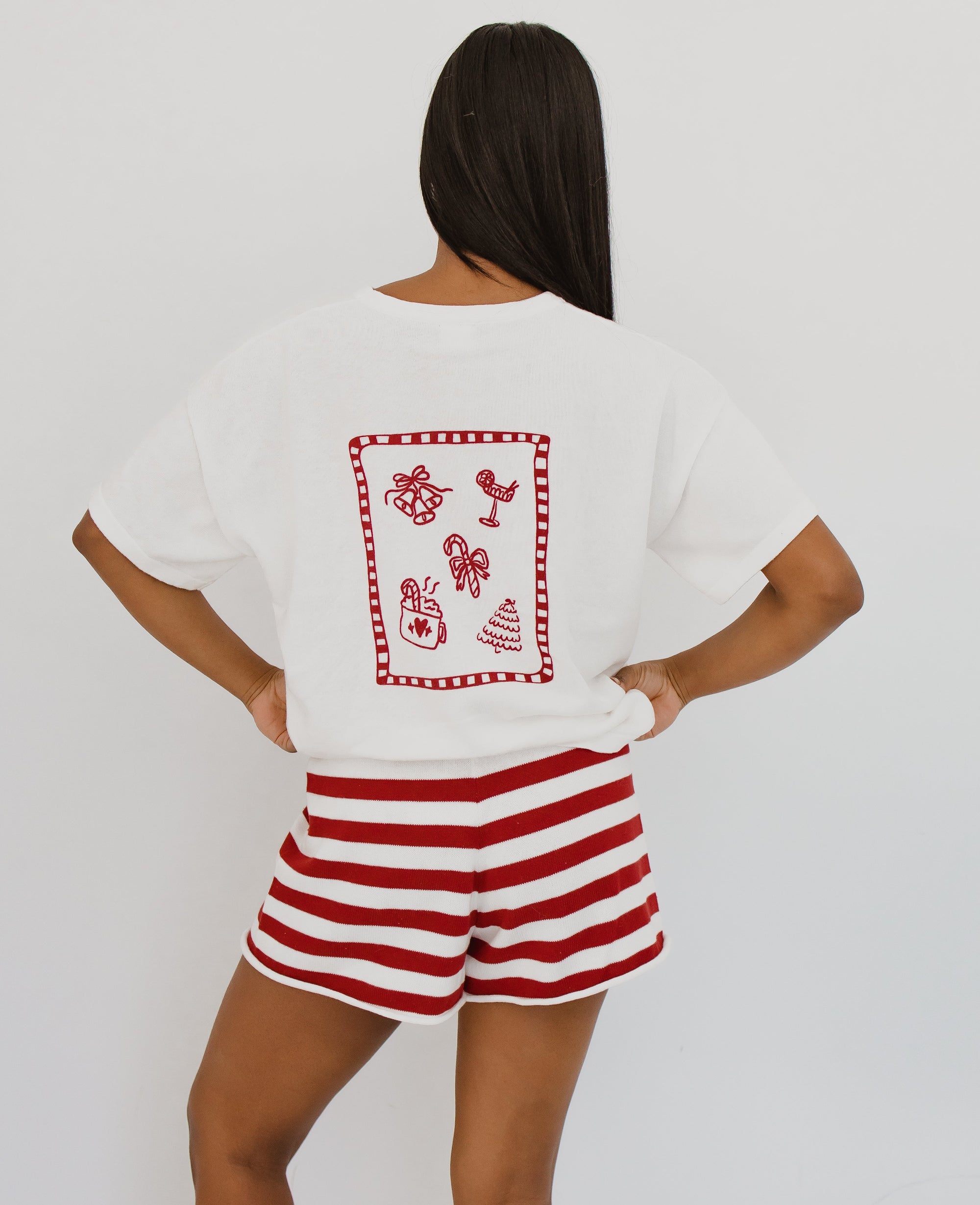 Back view of a women's white Christmas tee with a red doodle print of bells, candy canes and a tree