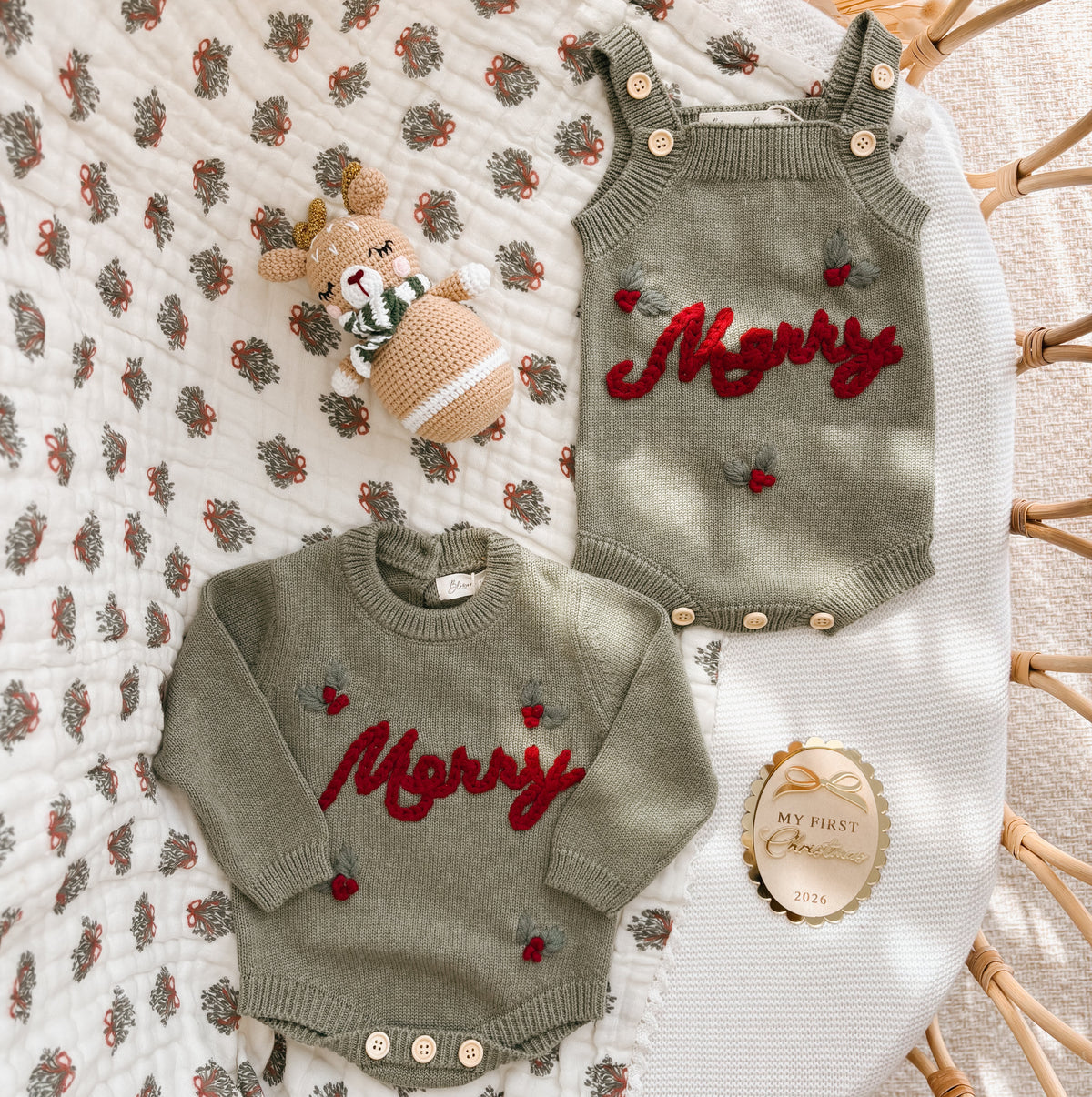 Sage green Merry knit overall romper and jumper romper laid out together with a crochet reindeer rattle and a My First Christmas 2026 keepsake disc