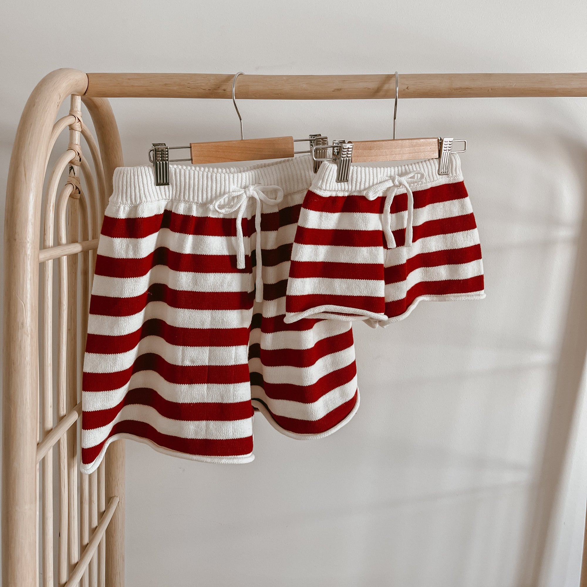 Matching adult and child red and white stripe knit Christmas shorts hanging on a rattan rack