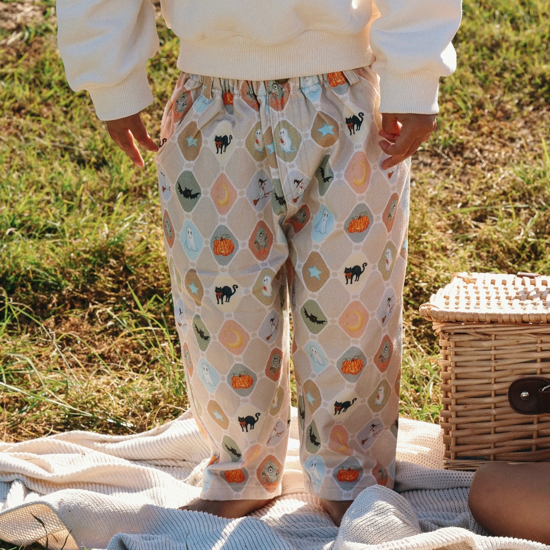 Close up of Halloween print pants with ghost, cat and pumpkin tiles worn with a cream sweatshirt