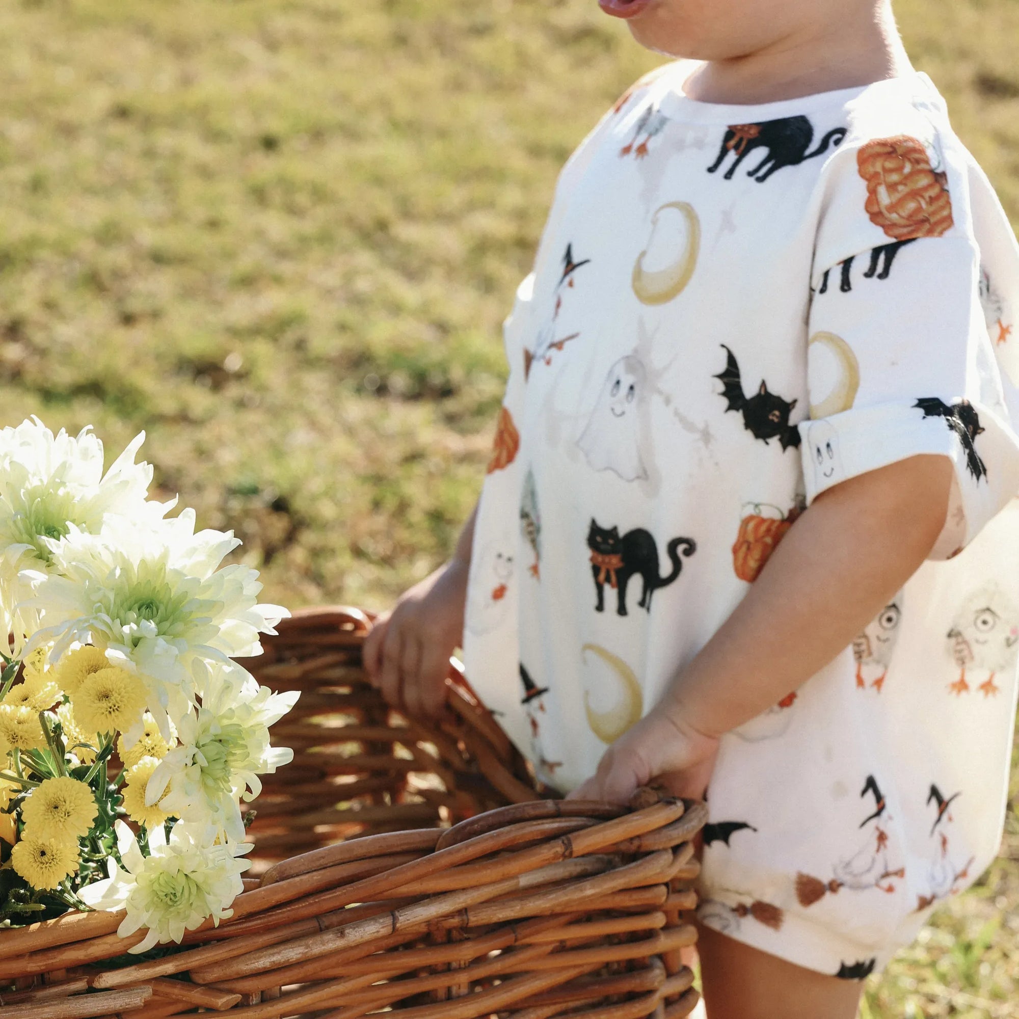Close up of a Halloween print bubble romper with ghosts, black cats and pumpkins beside a flower basket